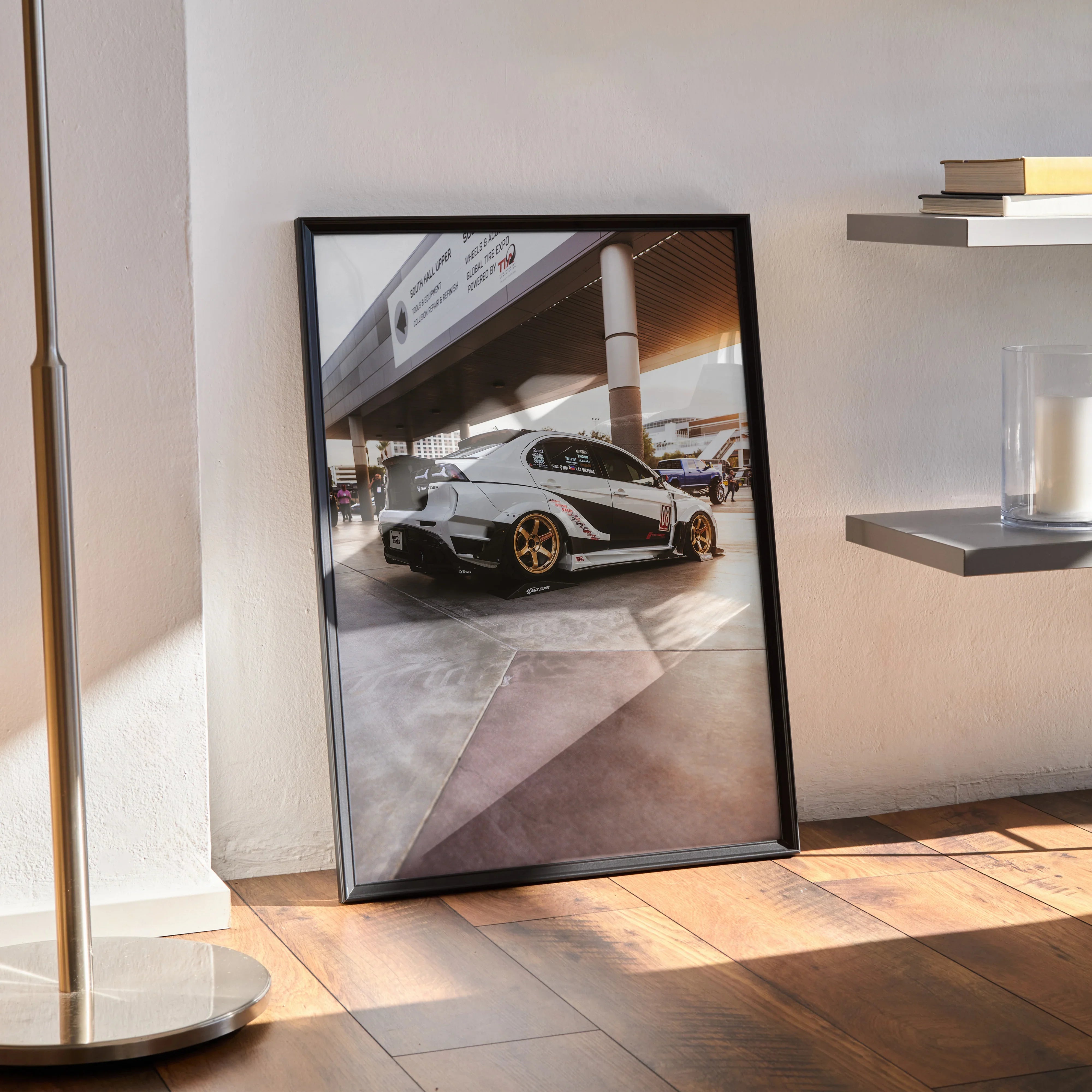 Mitsubishi Evo 10 poster wall art in black frame leaning on wall with gold wheels and sleek design.