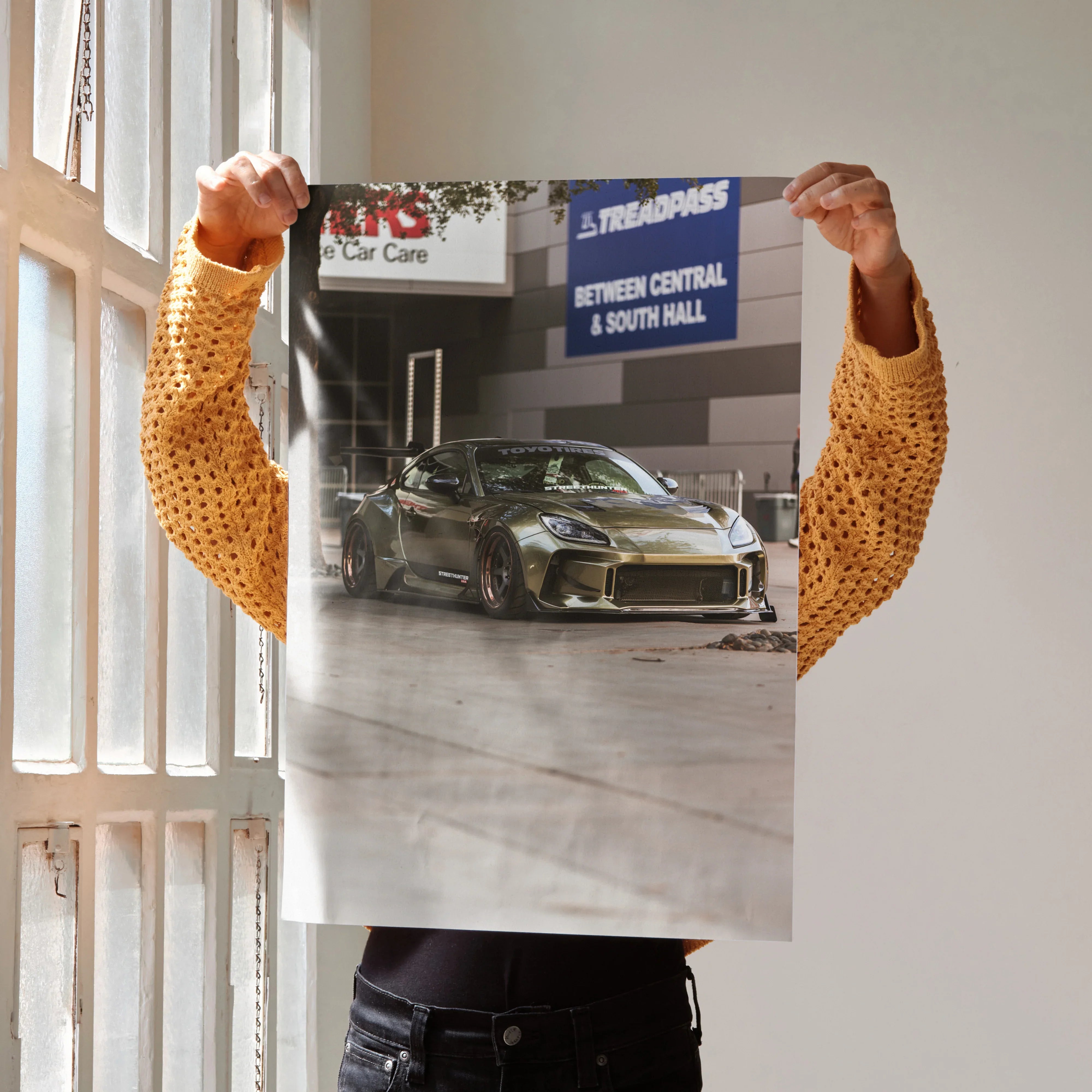 Subaru BRZ sports car poster with metallic green finish, satin wall art decor held by person in mustard sweater.