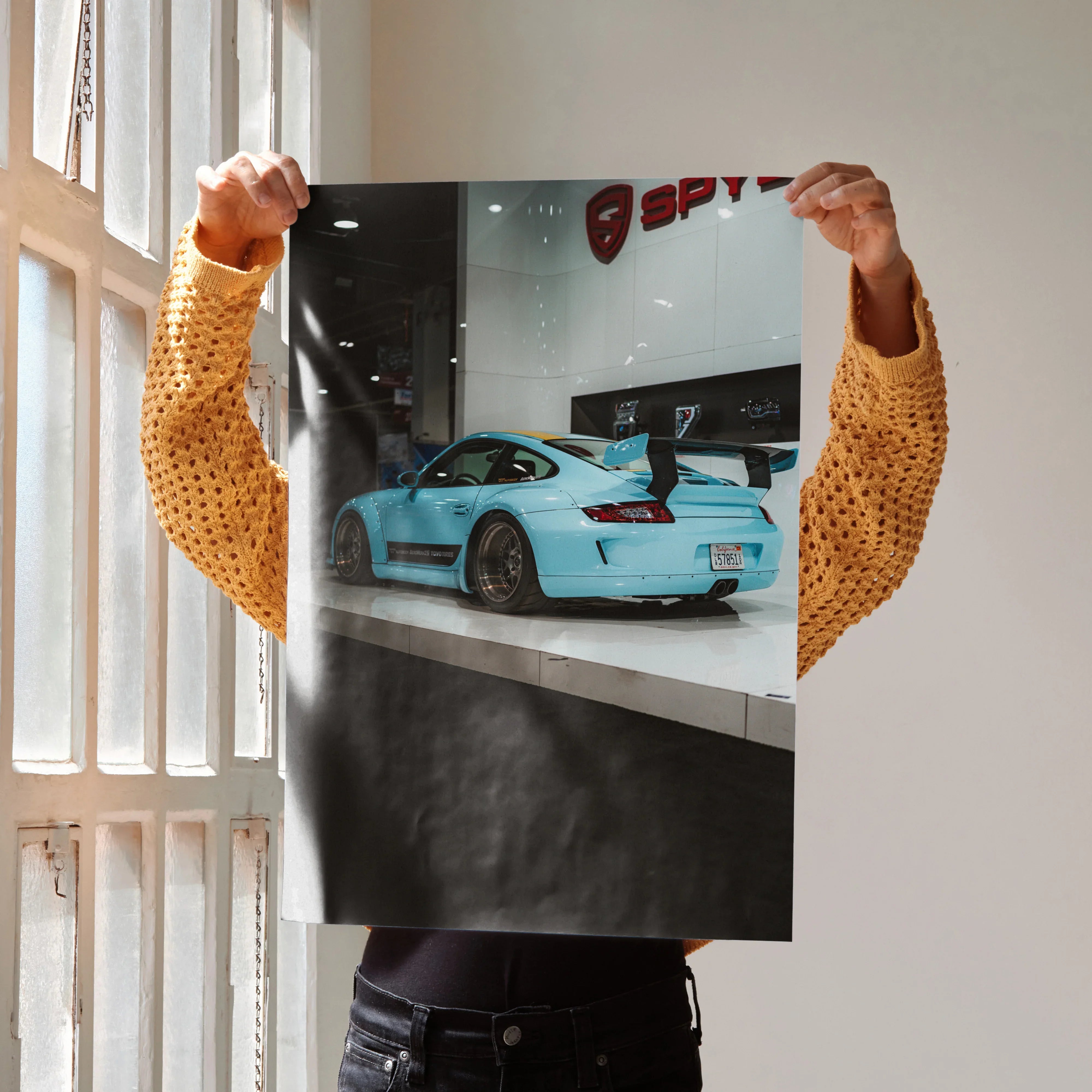 Porsche 911 Carrera 4 blue sports car poster held against light wall, high-resolution wall art.