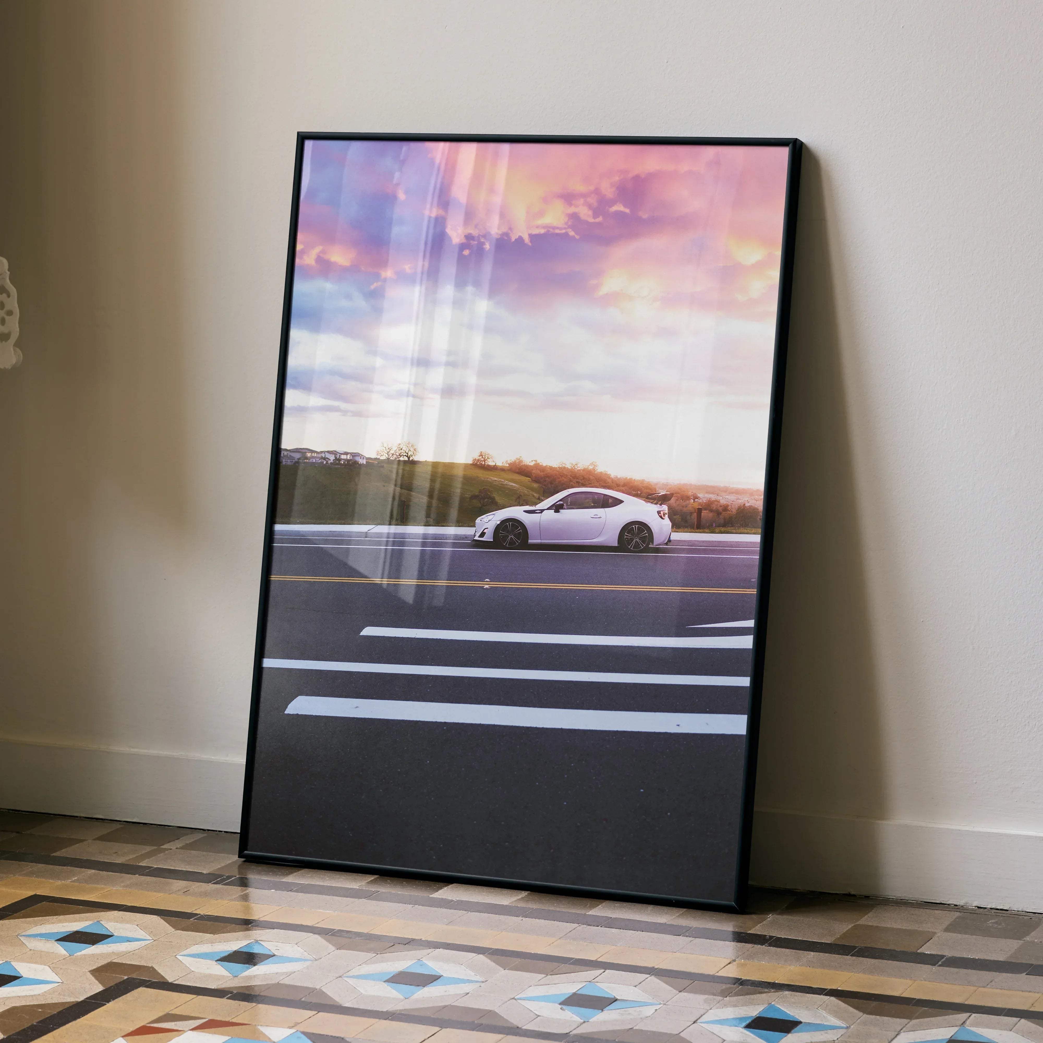 A framed poster of a white toyota frs sports car on a road under a vibrant pink and purple sunset sky
