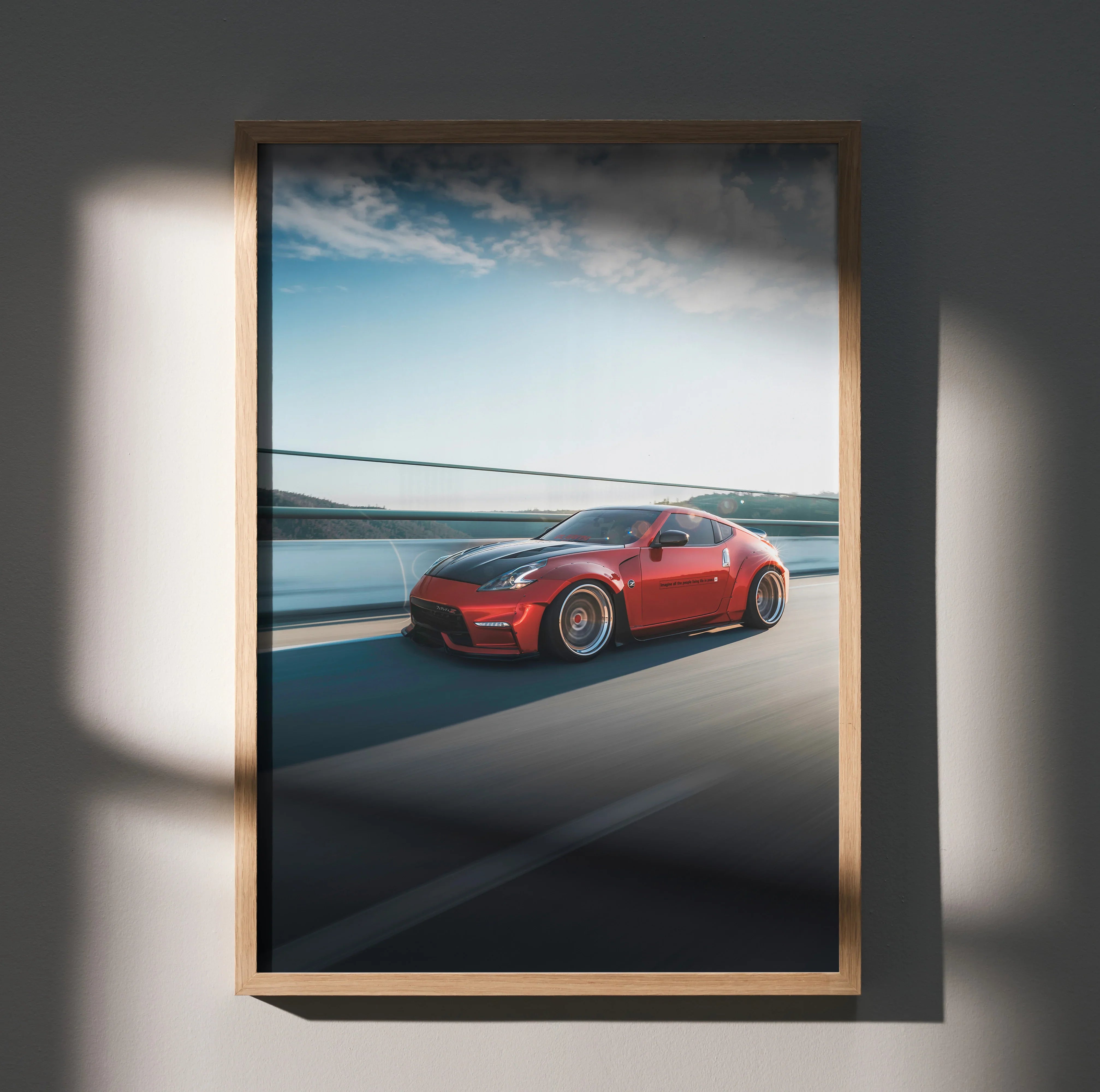 Red Nissan 370Z driving on coastal road wall art poster in wooden frame.