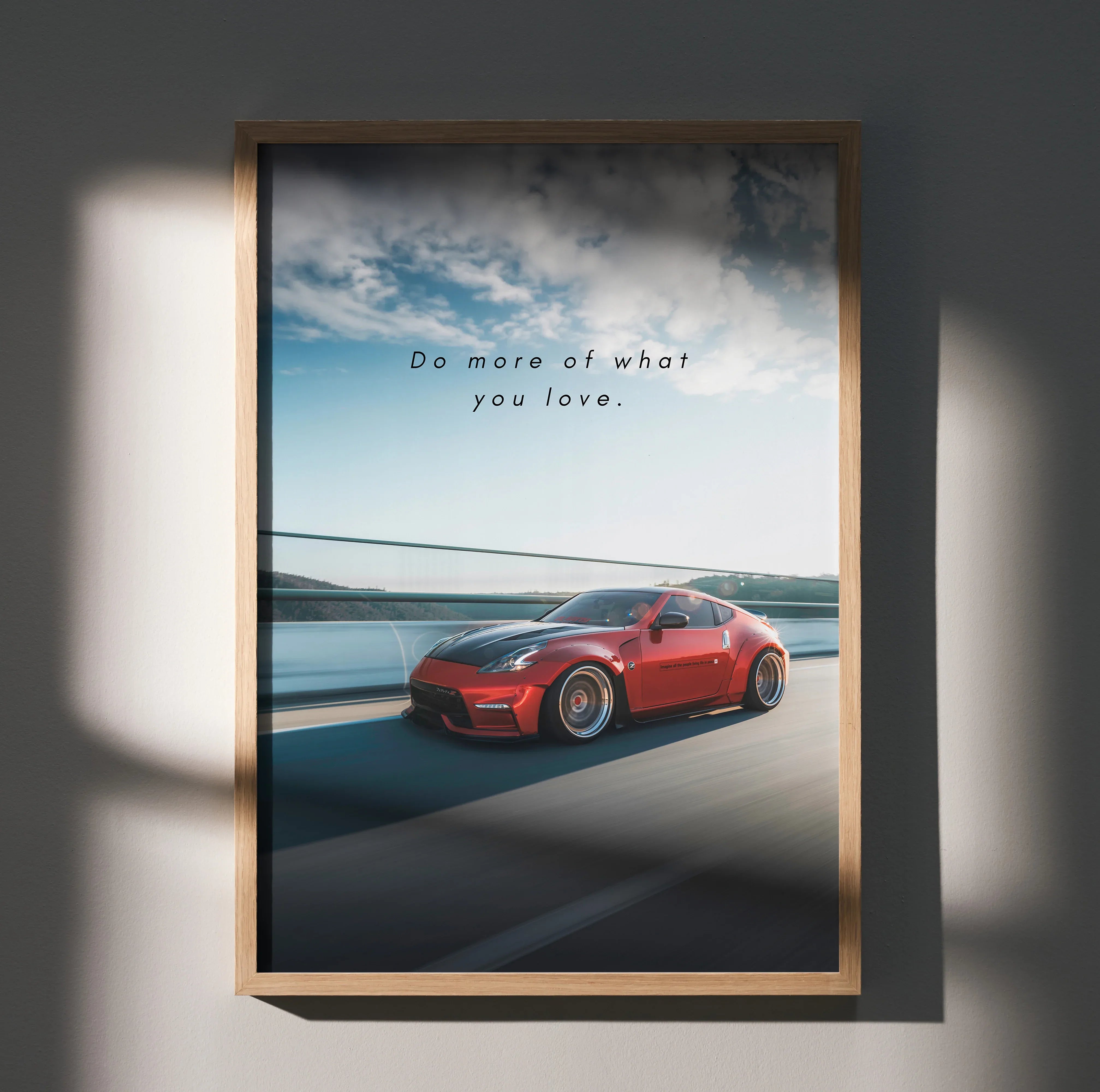 Motivational poster wall art featuring a red Nissan 370z with inspiring text "Do more of what you love" against a cloudy sky .