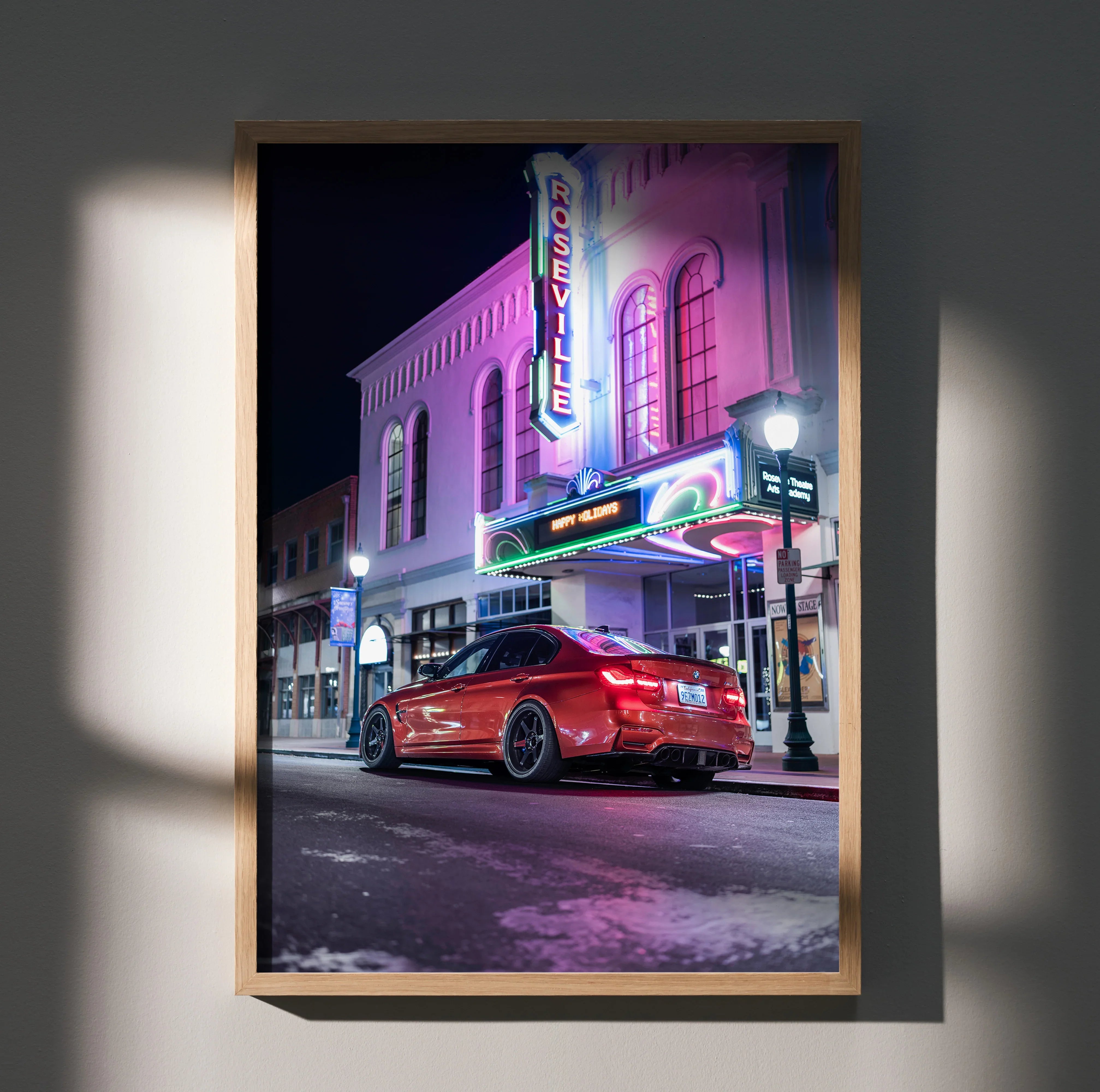 Poster wall art featuring a red BMW F80 M3 parked in front of a neon-lit theater at night.