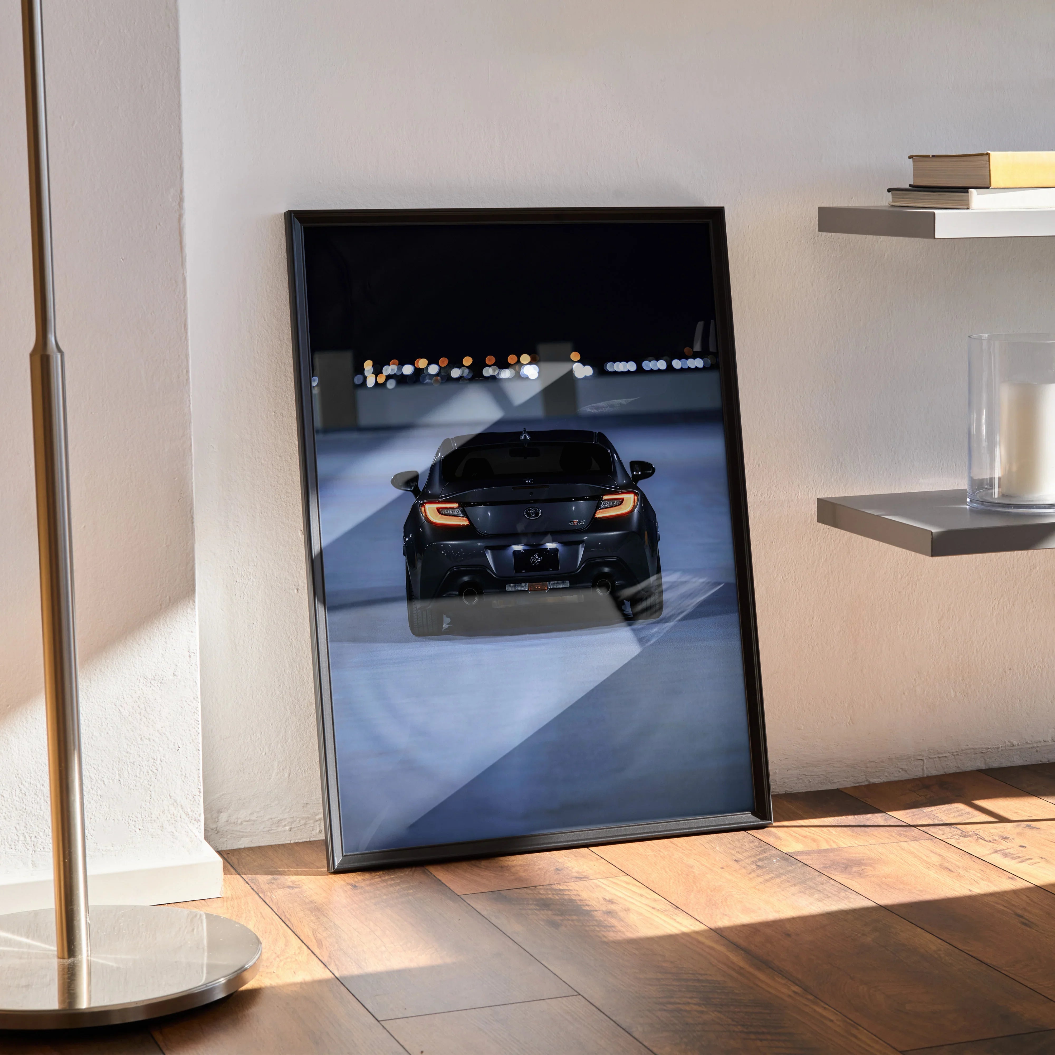 Toyota GR86 black sports car poster framed on floor, modern wall art with city lights backdrop.