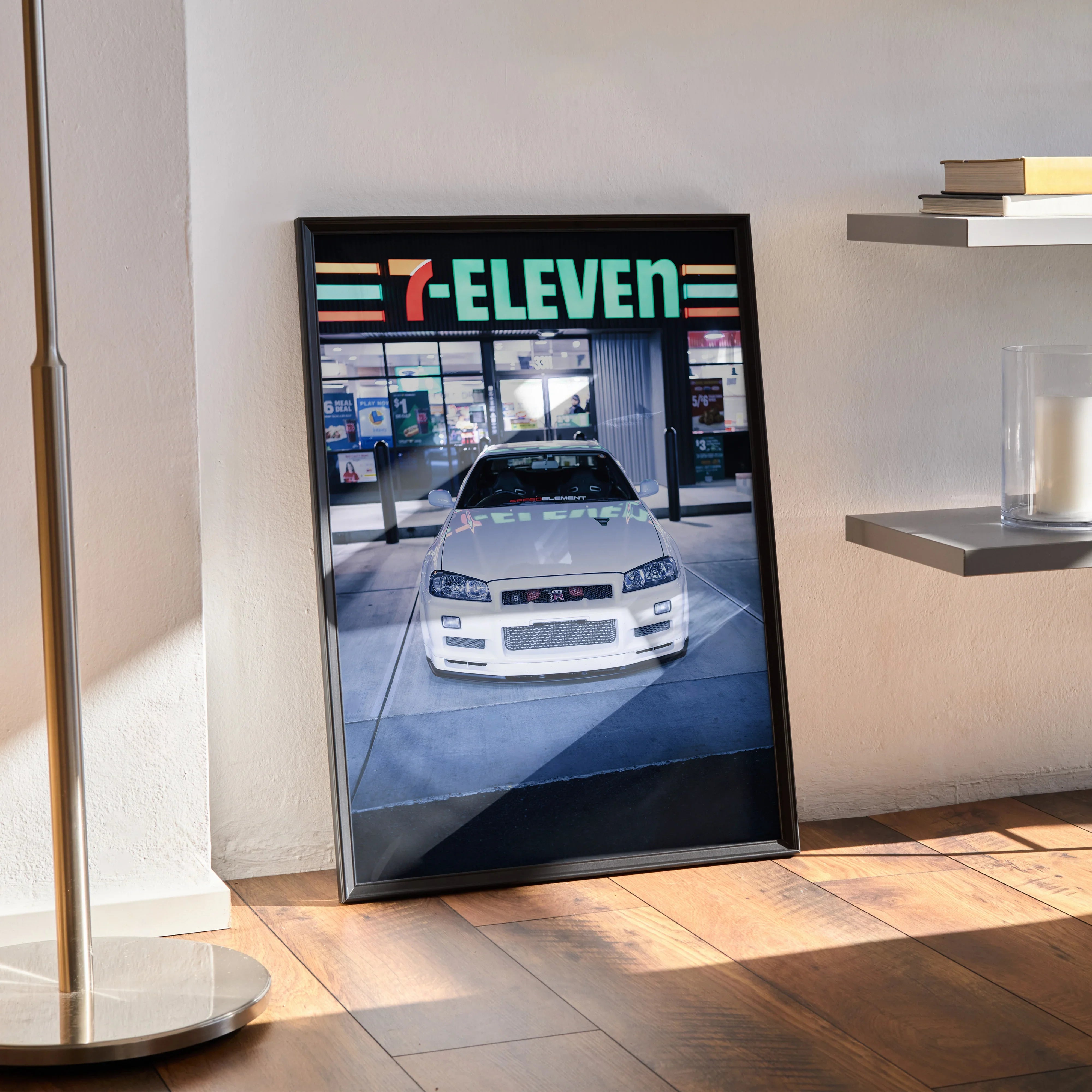 Nissan R34 GTR poster with 7-Eleven storefront in background, framed wall art in modern room setting.
