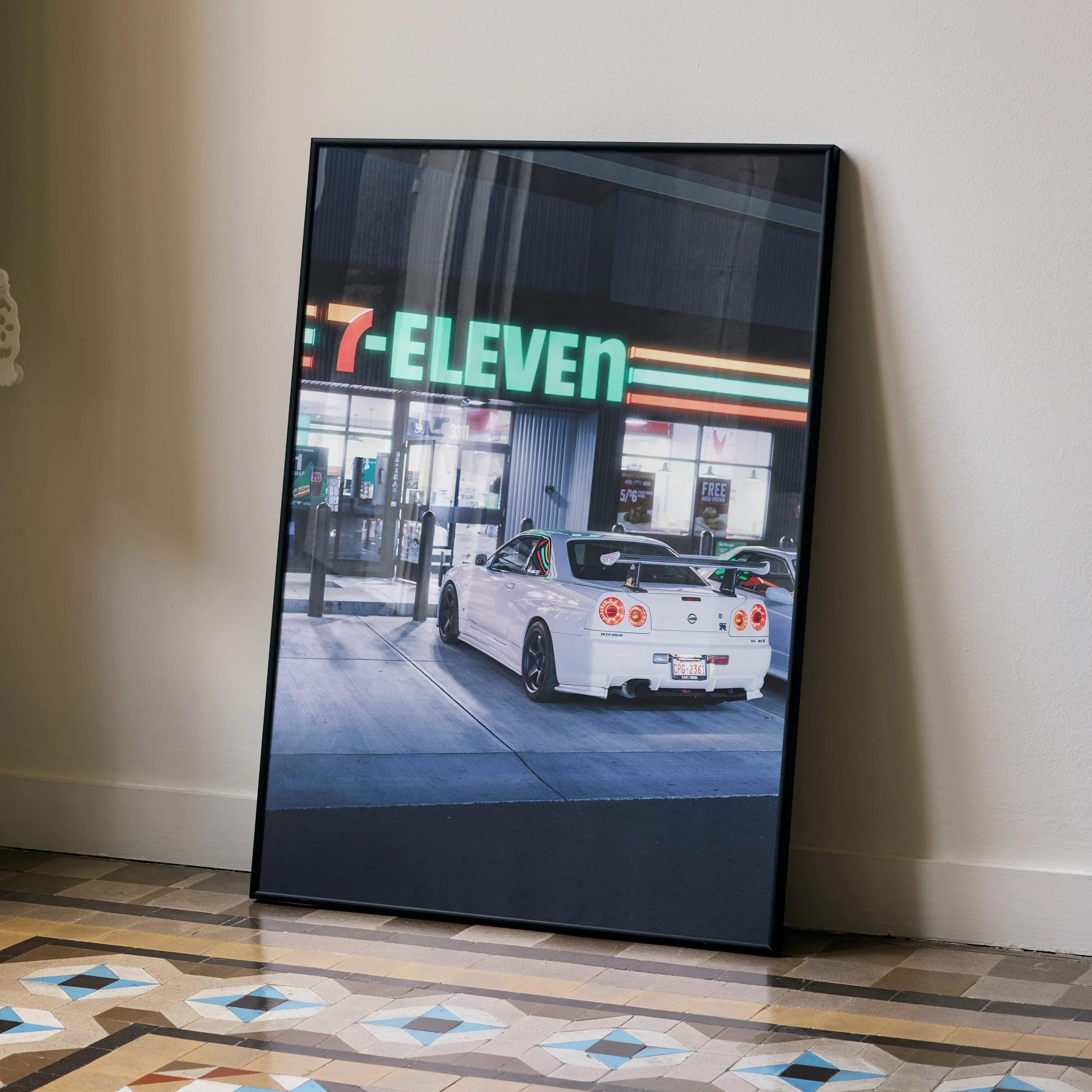 Black-framed canvas print of a white nissan gtr r34 skyline parked by a glowing green 7-eleven sign automotive decor