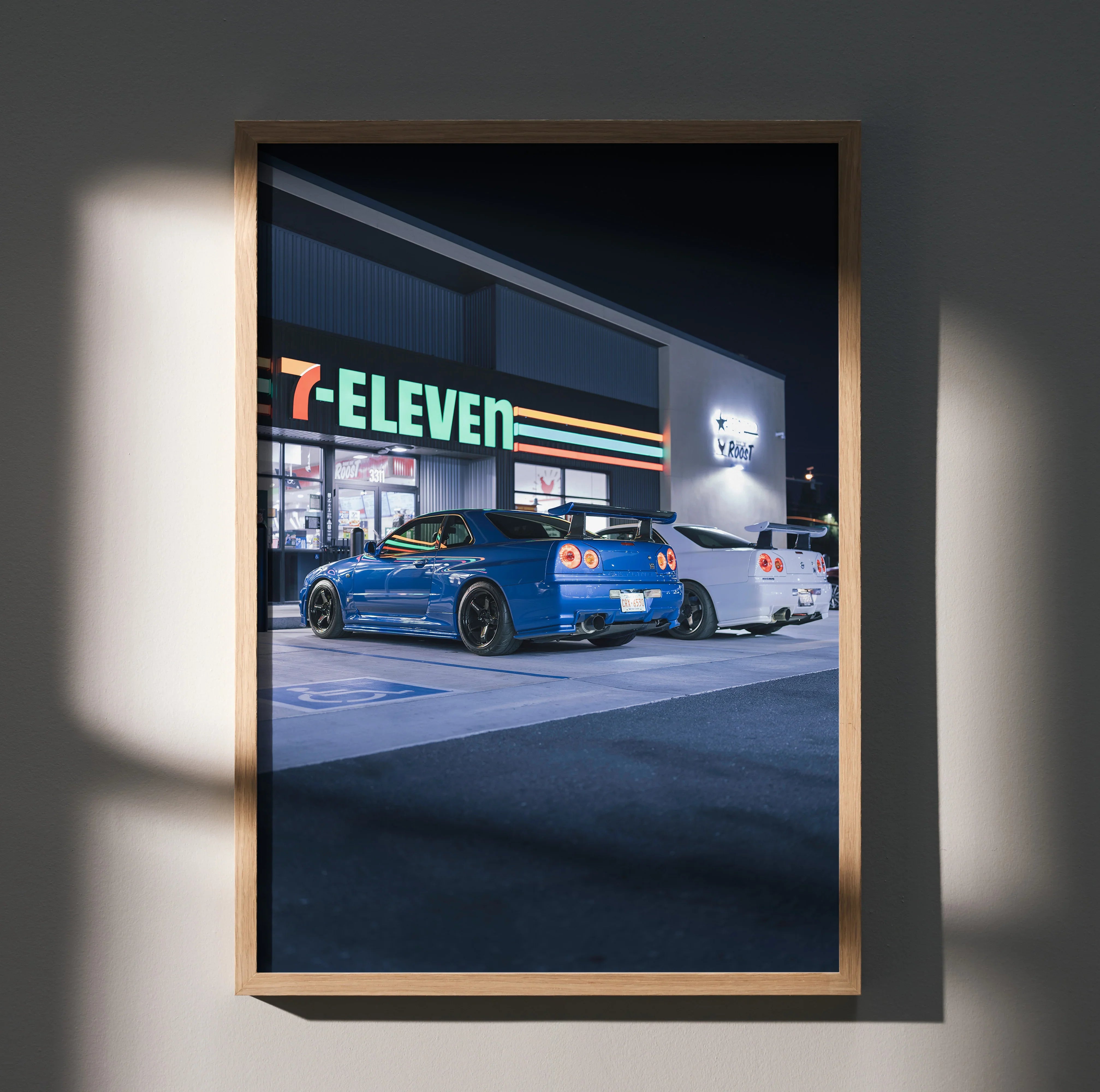 Nissan R34 GTR in blue parked outside 7-Eleven at night poster wall art in wooden frame.