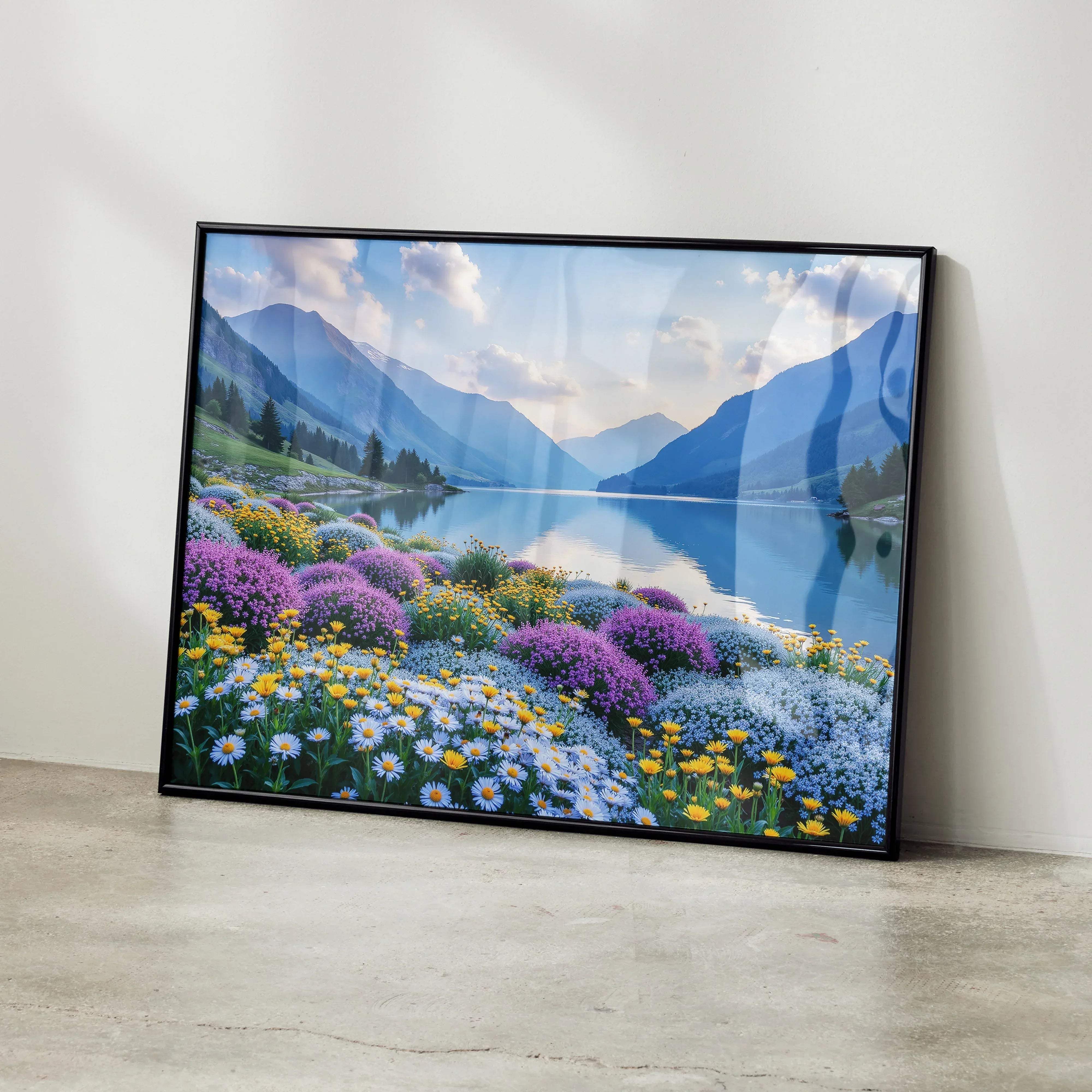 Black-framed landscape print of vibrant purple yellow and white flowers by a lake with mountains and a cloudy sky