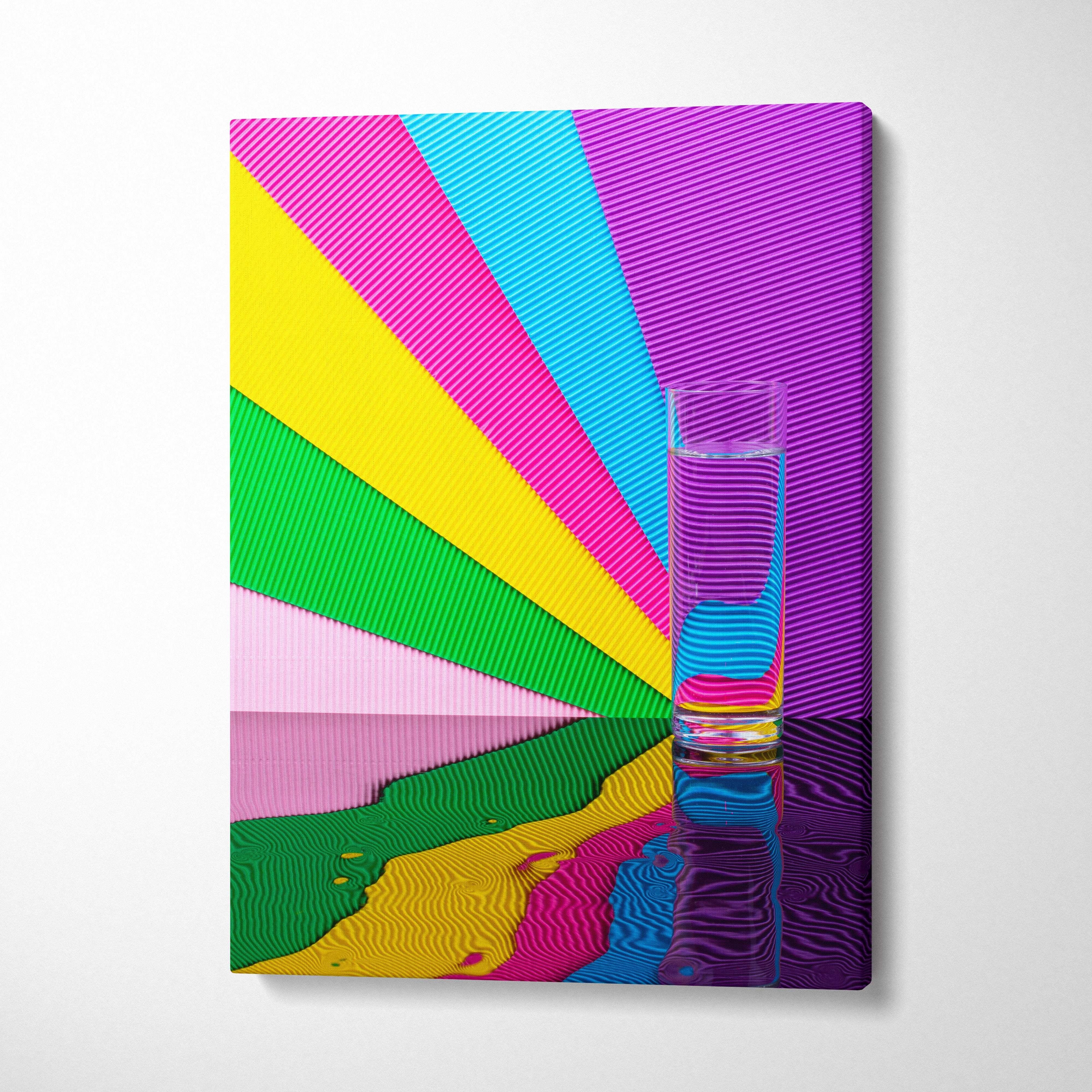 A clear glass tumbler filled with water on a reflective surface with vibrant multi-colored striped rainbow glass wall art