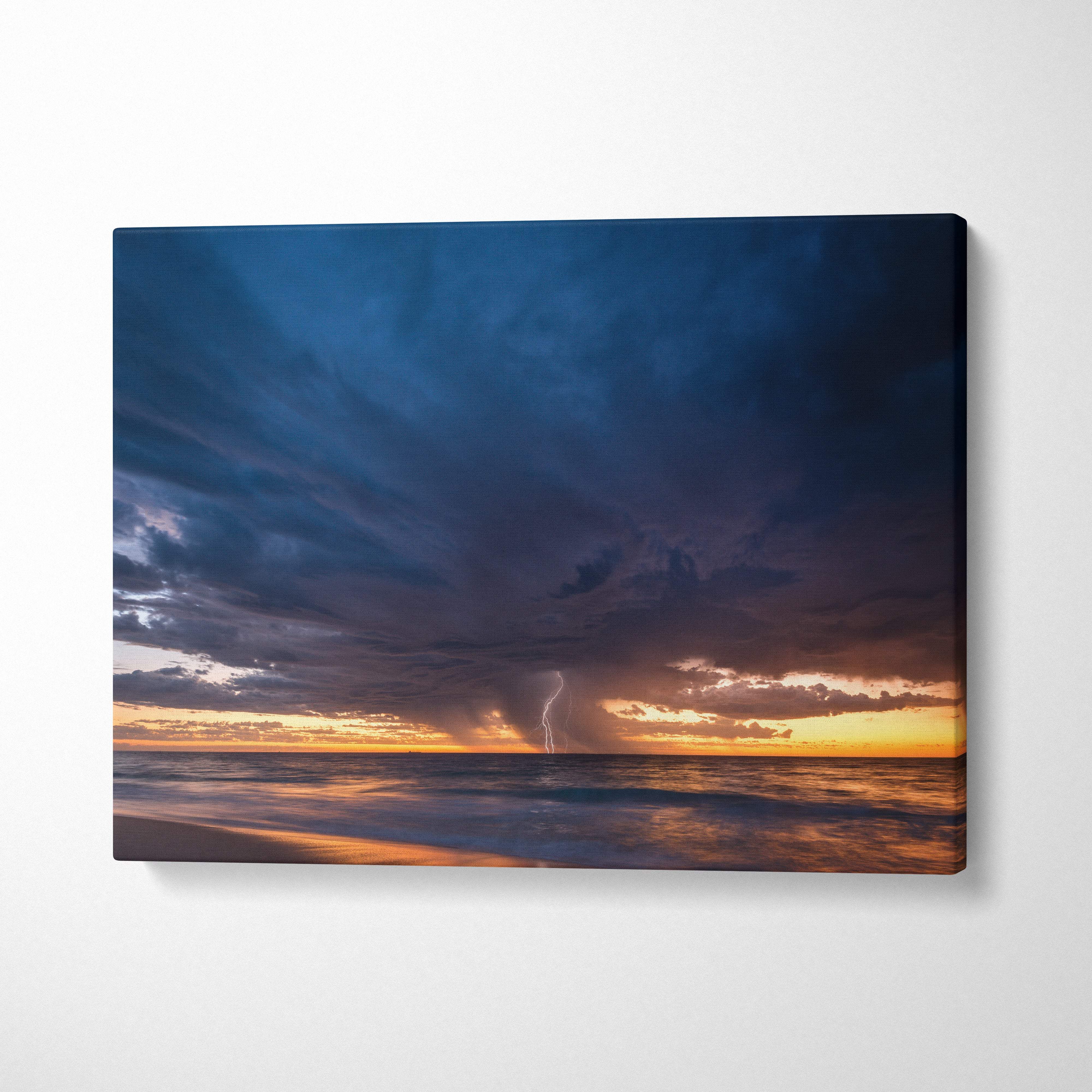 Canvas print of a stormy ocean sunset with deep blue clouds and lightning illuminating the golden horizon wall decor