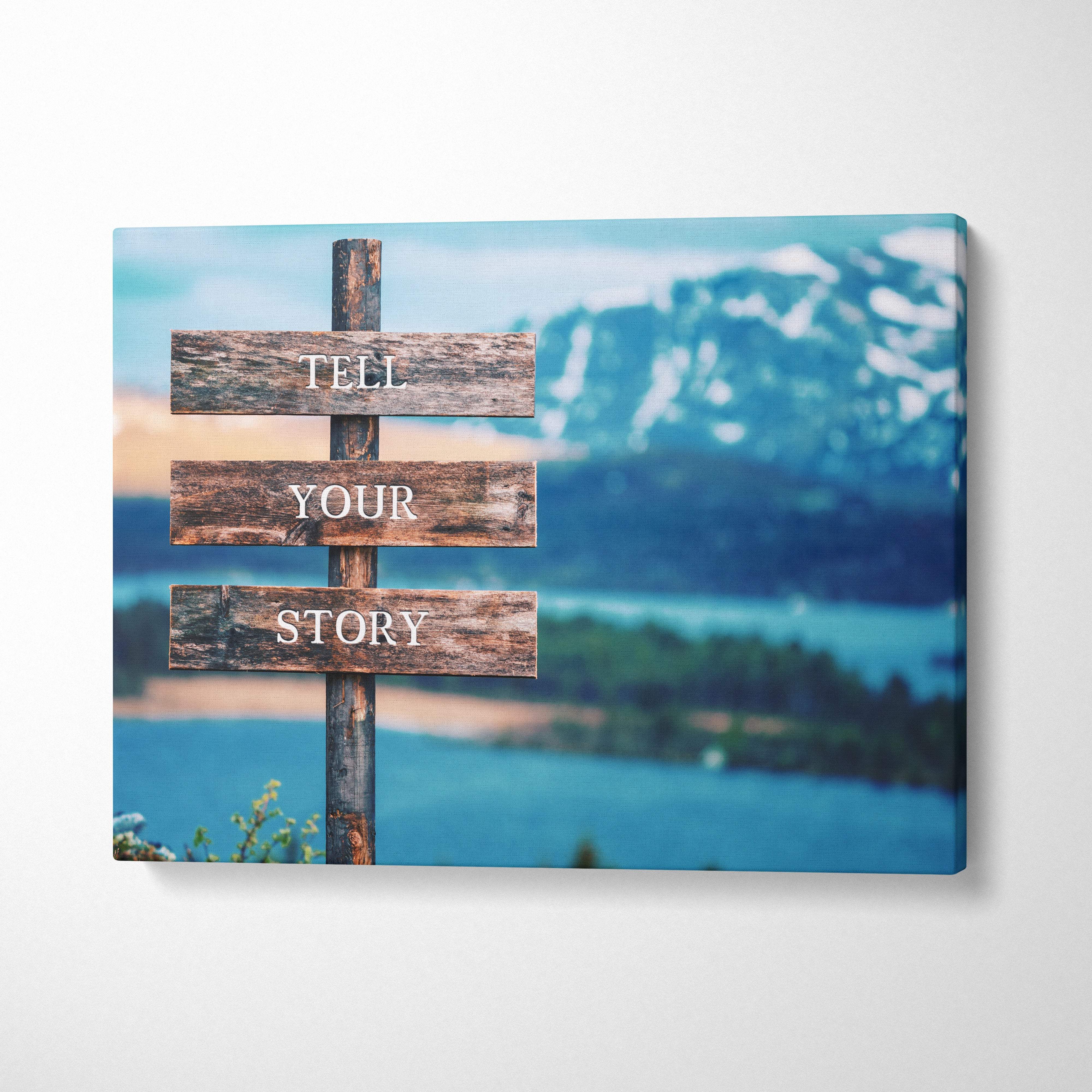 Motivational tell your story canvas wall art featuring a rustic blue wooden signpost with white lettering and mountain lake backdrop