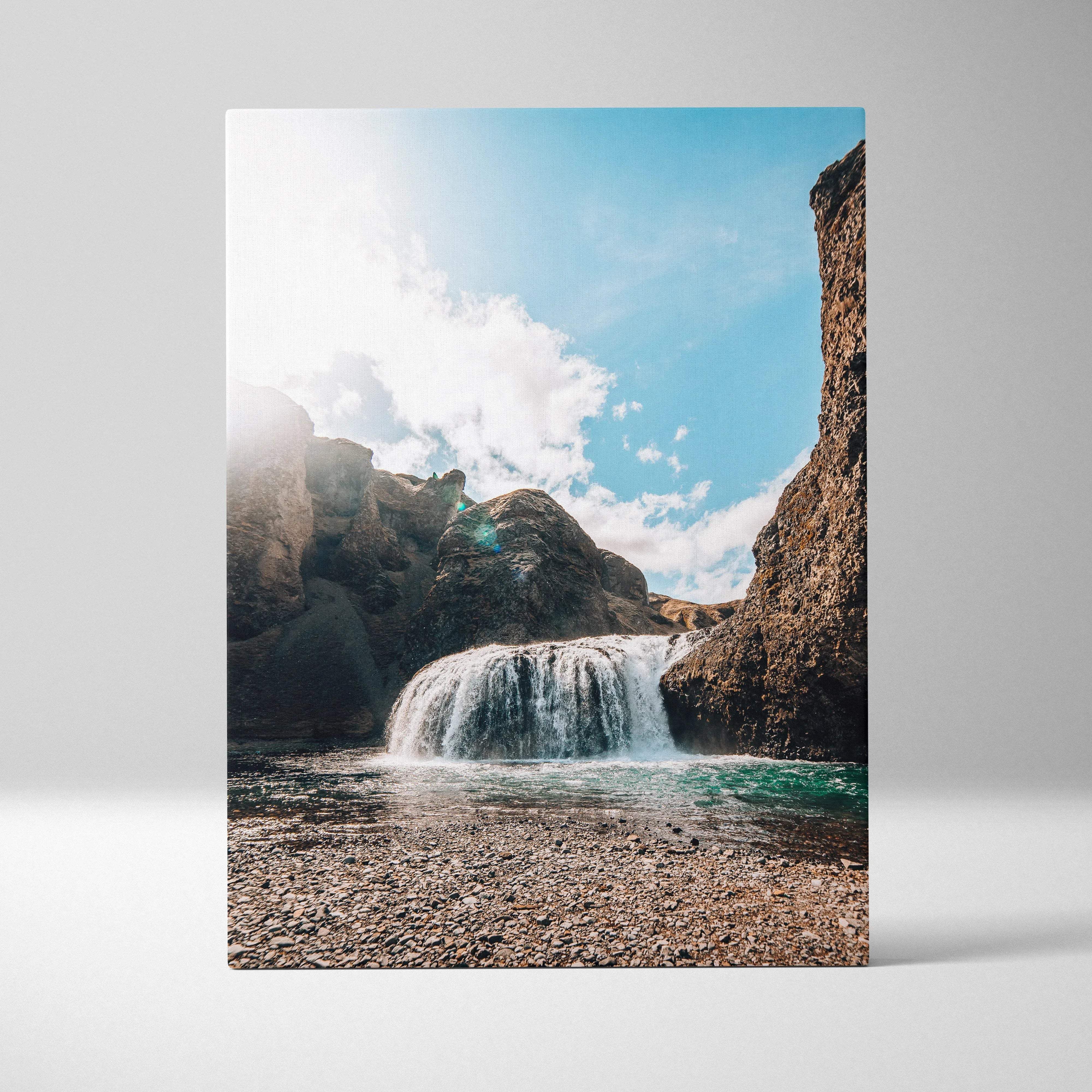 A rectangular canvas print of a vibrant icelandic waterfall over sunlit rocks with bright blue sky and scattered clouds