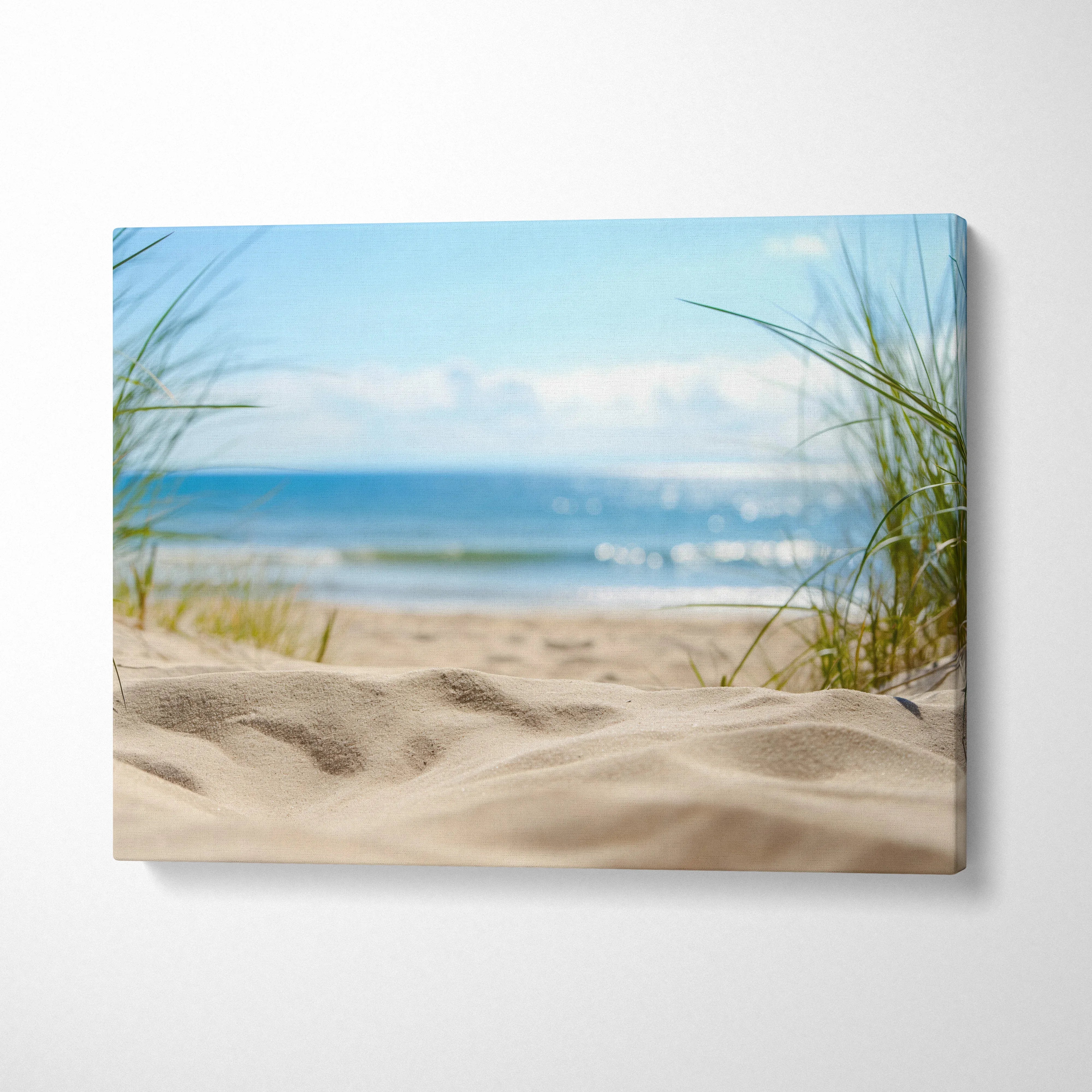 Canvas wall art depicting sunlit sandy beach with grass tufts and calm ocean waves under a blue sky.
