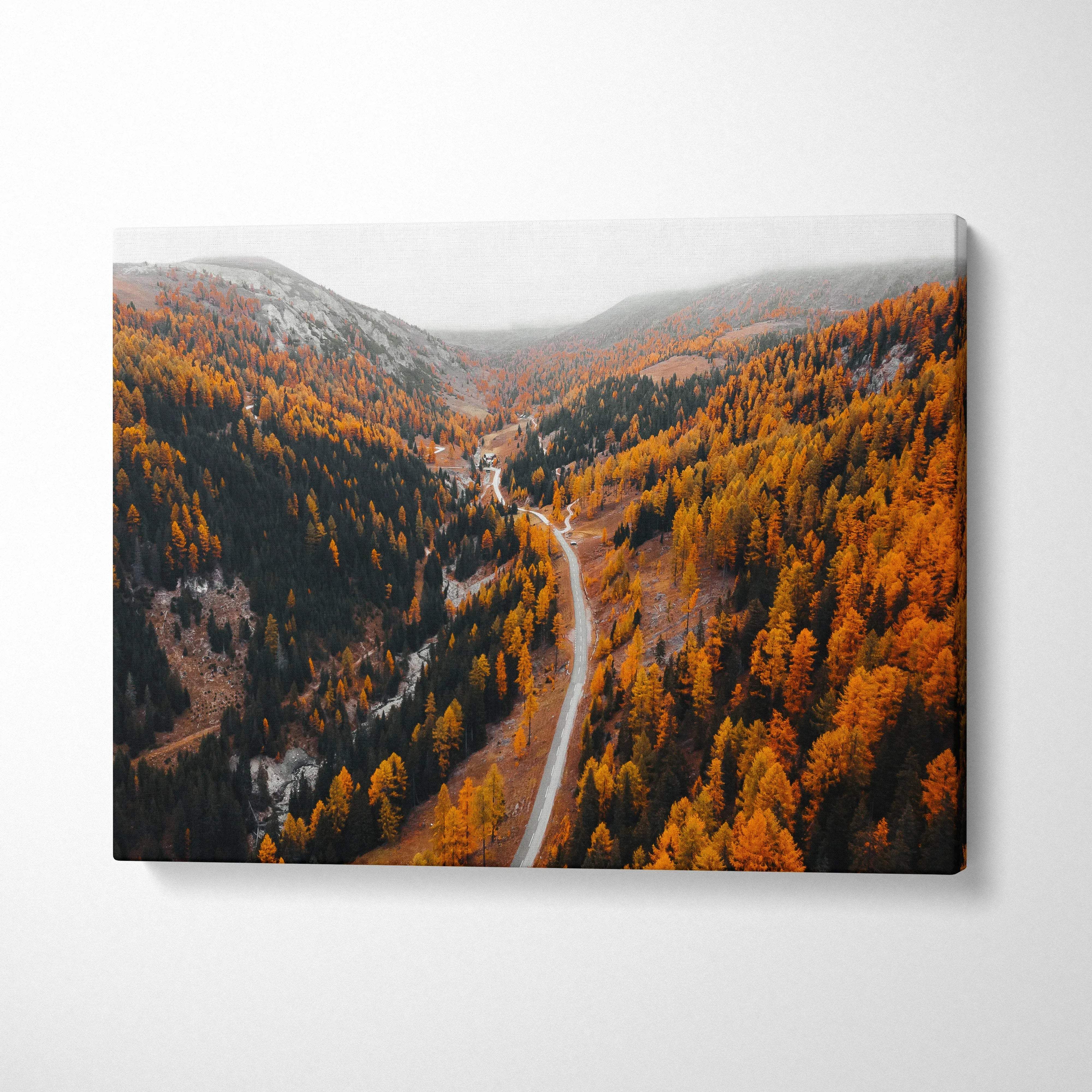 Autumn road winding through vibrant orange forest on canvas wall art with clear blue sky.