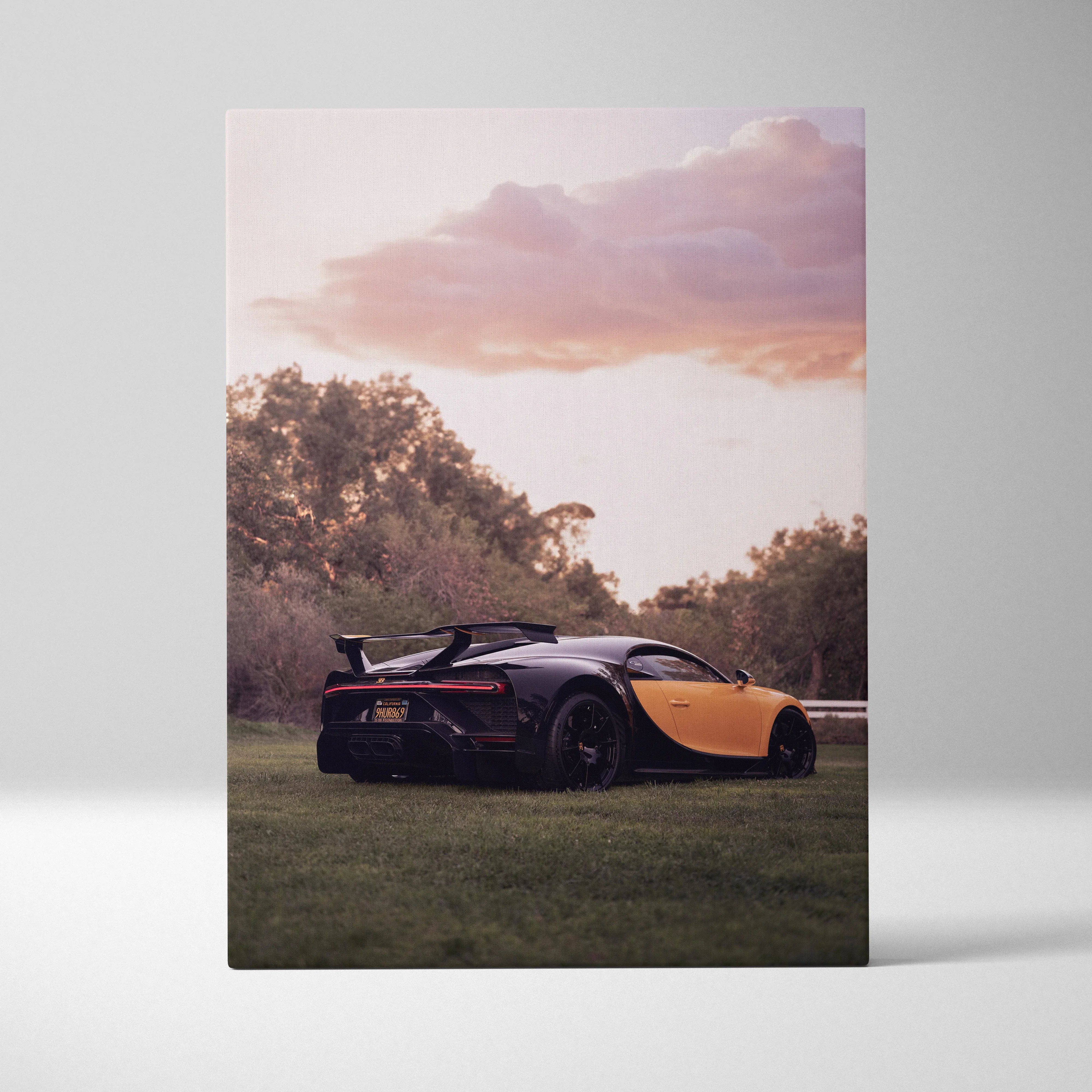 Vertical canvas wall art of a black and yellow Bugatti Chiron at sunset with trees in the background.