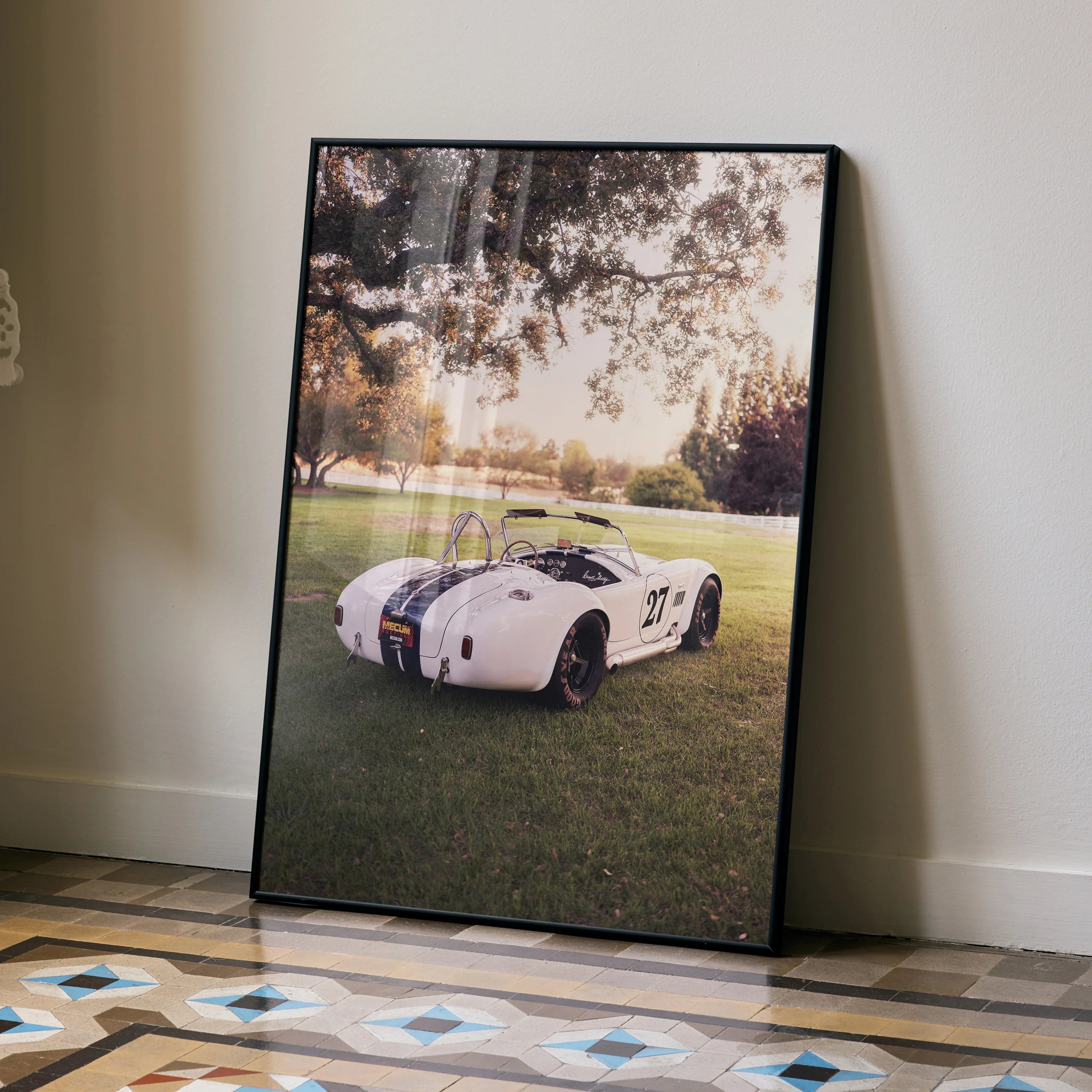 Shelby Cobra vintage car poster wall art in black frame leaning against beige wall.