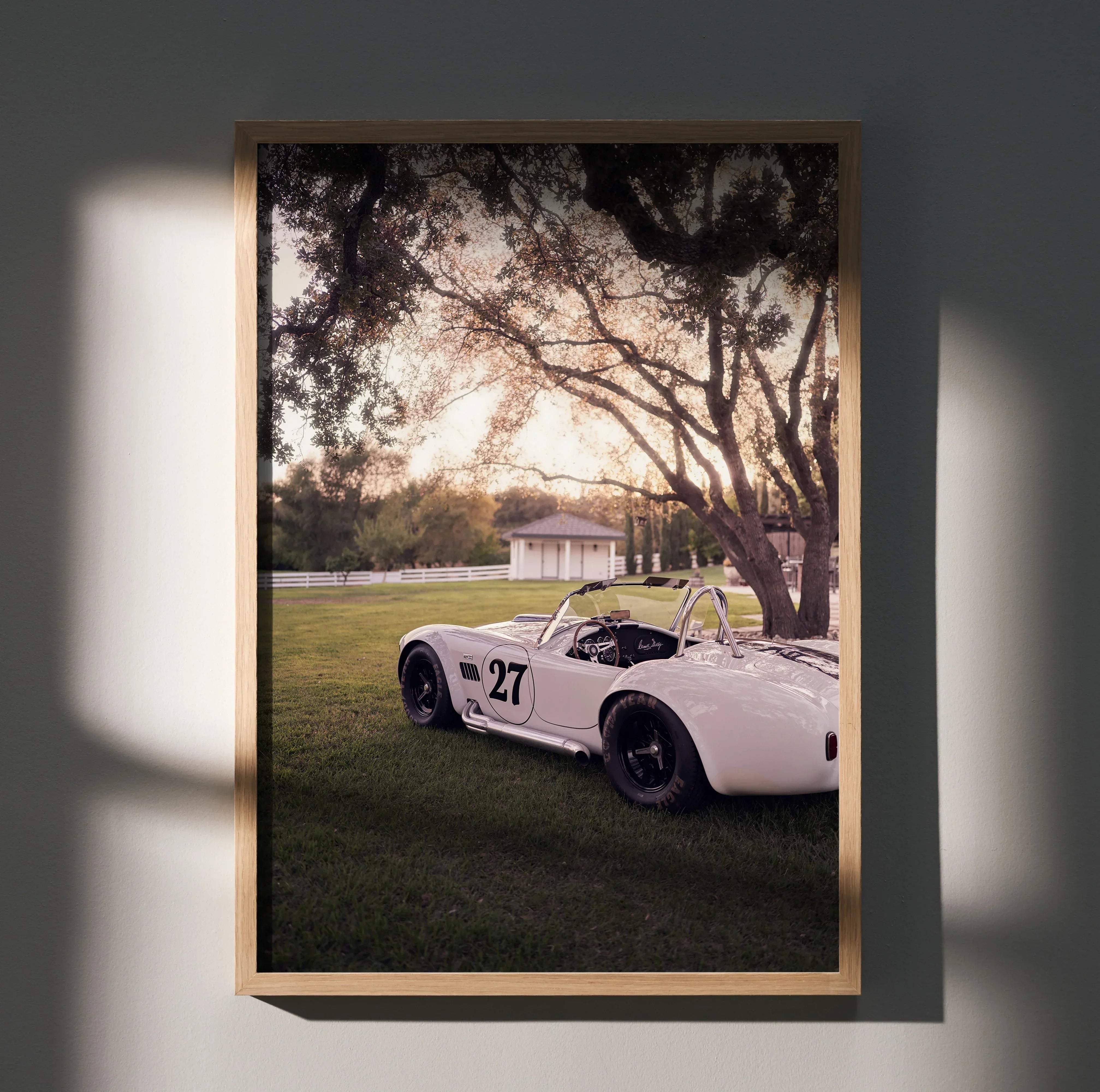 A framed photograph of a white vintage number 27 race car under trees in a sunlit field for automotive art poster