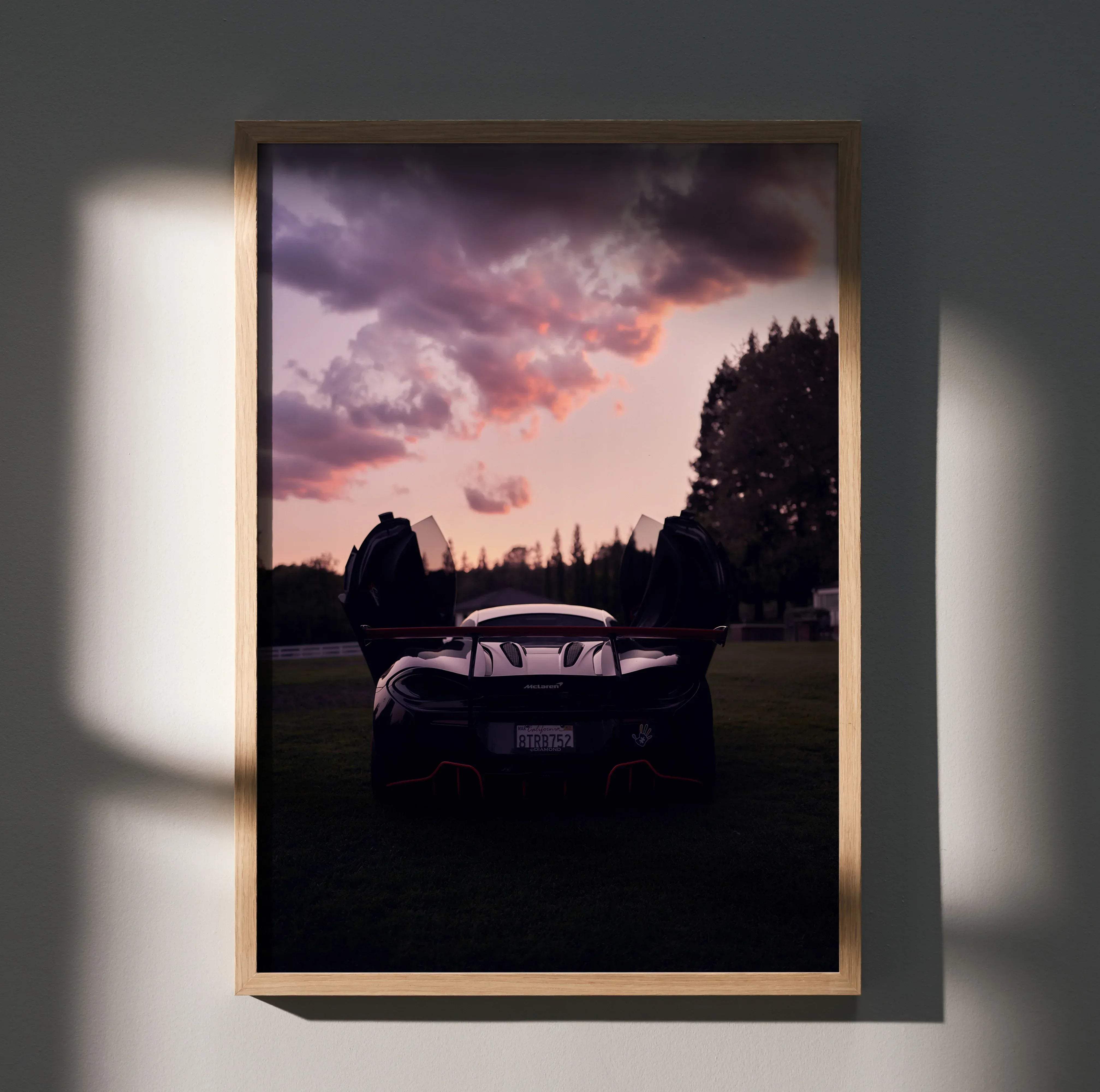 A framed poster of a black McLaren 570s sports car with open doors against a purple and pink sunset sky for home decor