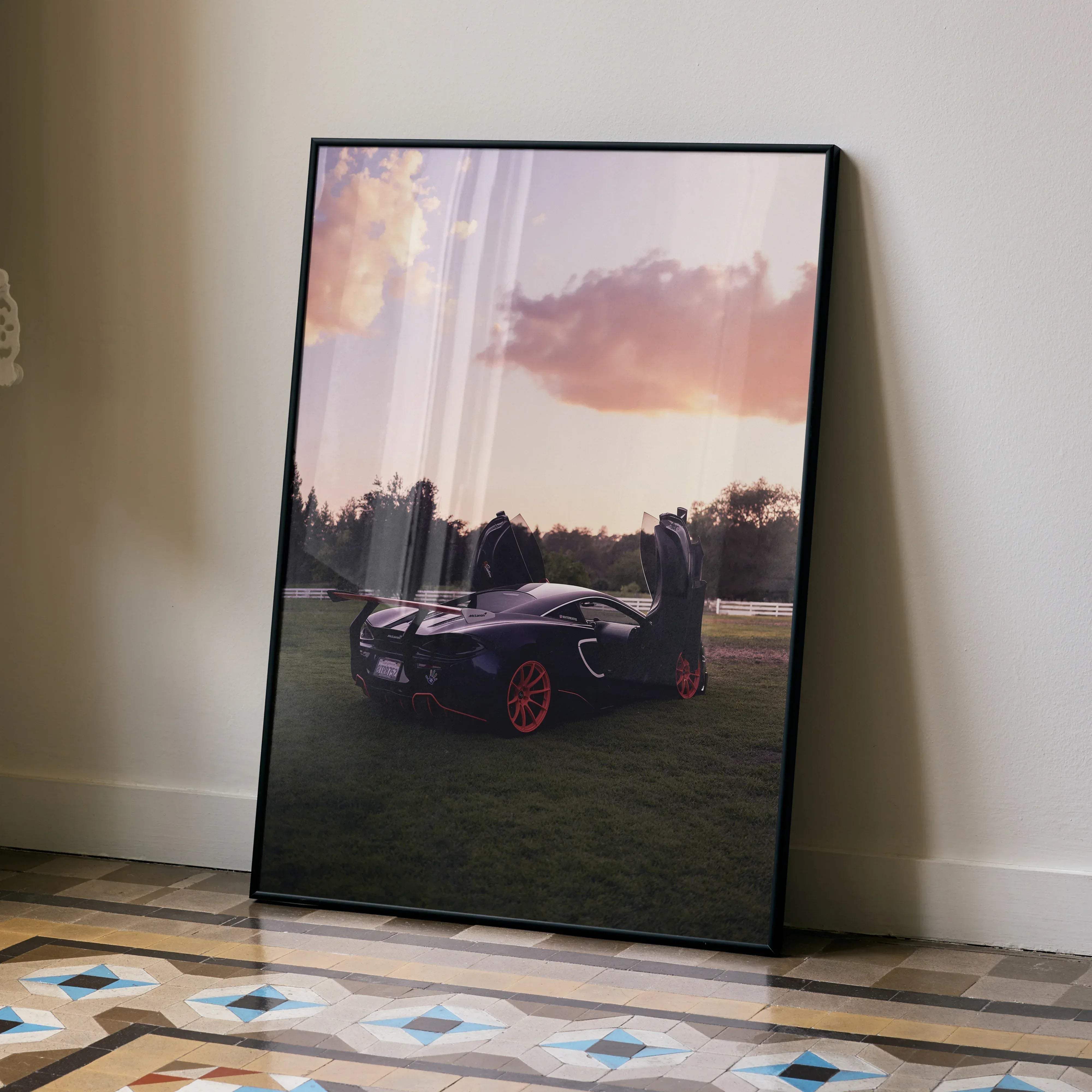 Black-framed McLaren 570s automotive art poster featuring a sleek black sports car with red wheels at sunset
