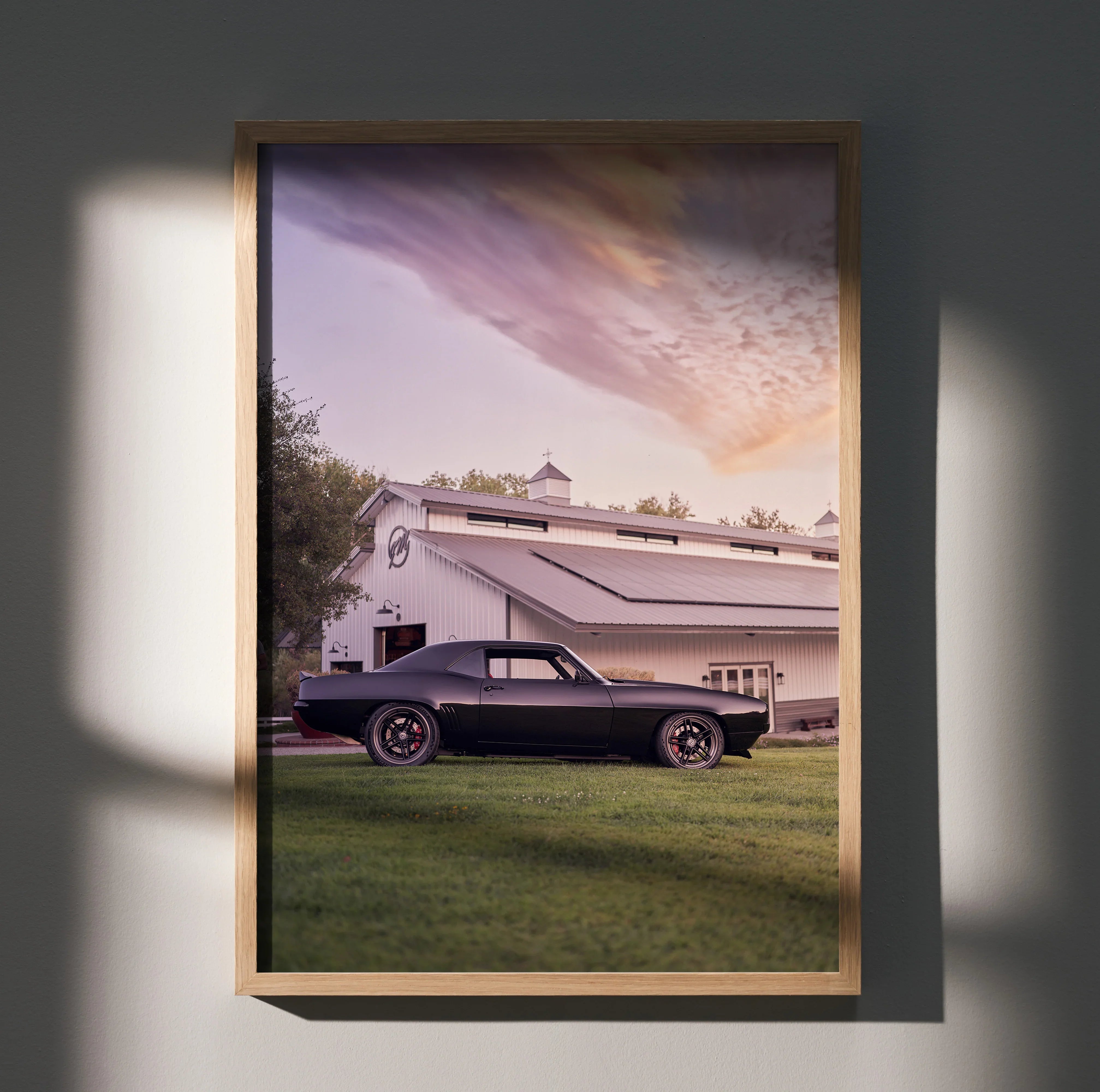 1969 black Camaro parked on grass in front of white barn under colorful sunset sky wall art poster.