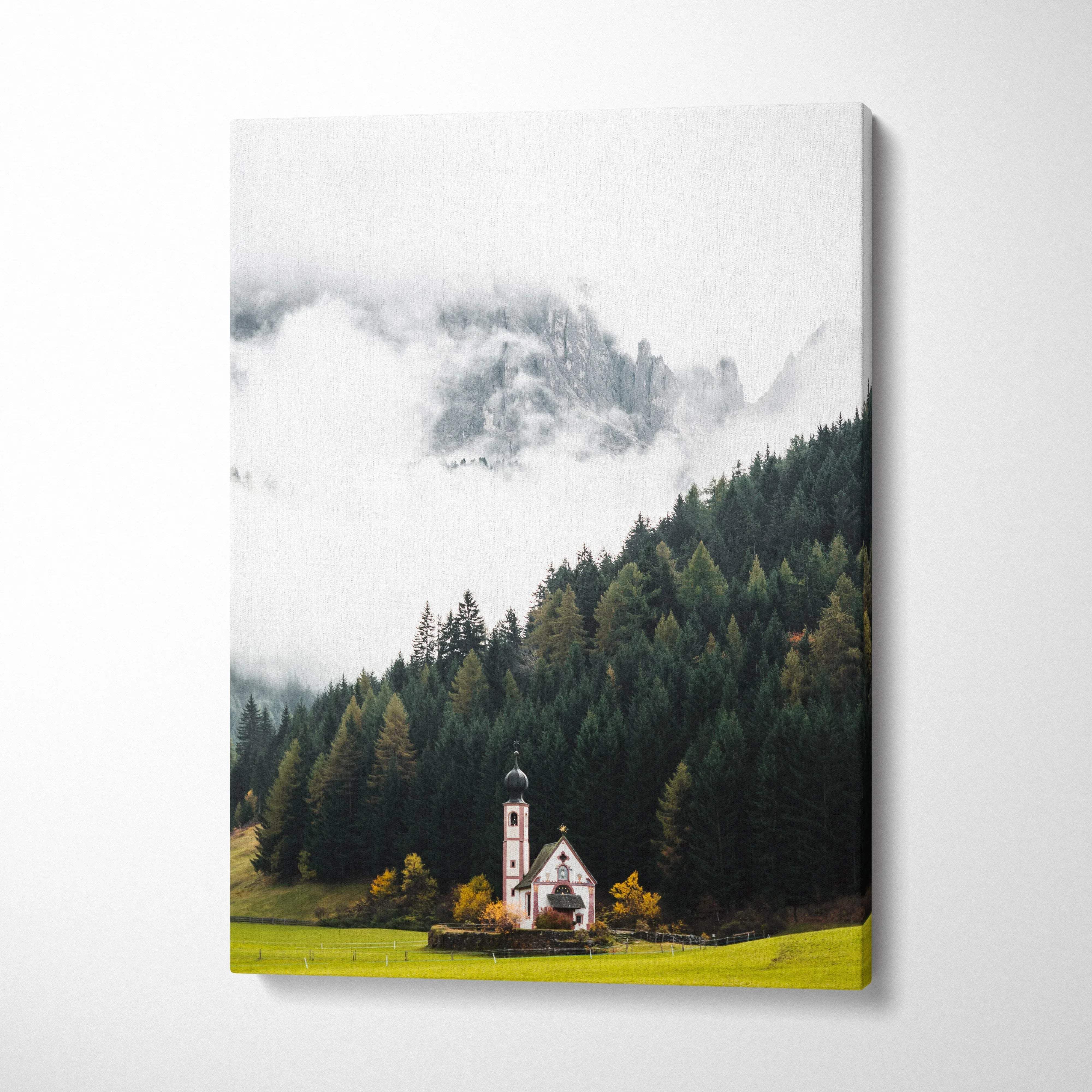 Vertical canvas wall art of a small church in a misty forest with mountains in the background.
