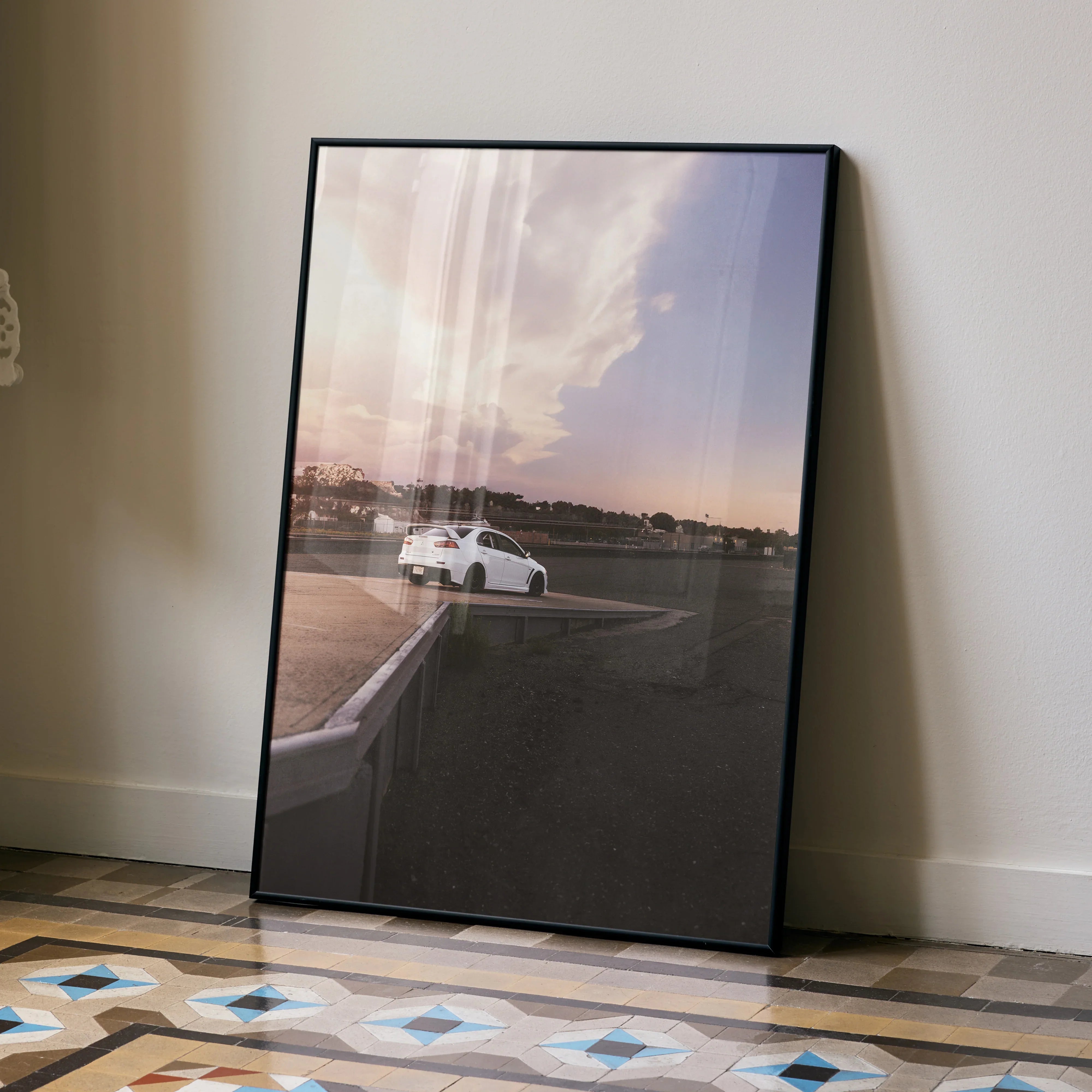 Mitsubishi Evo 10 poster wall art with sunset car photo in black frame leaning on wall.