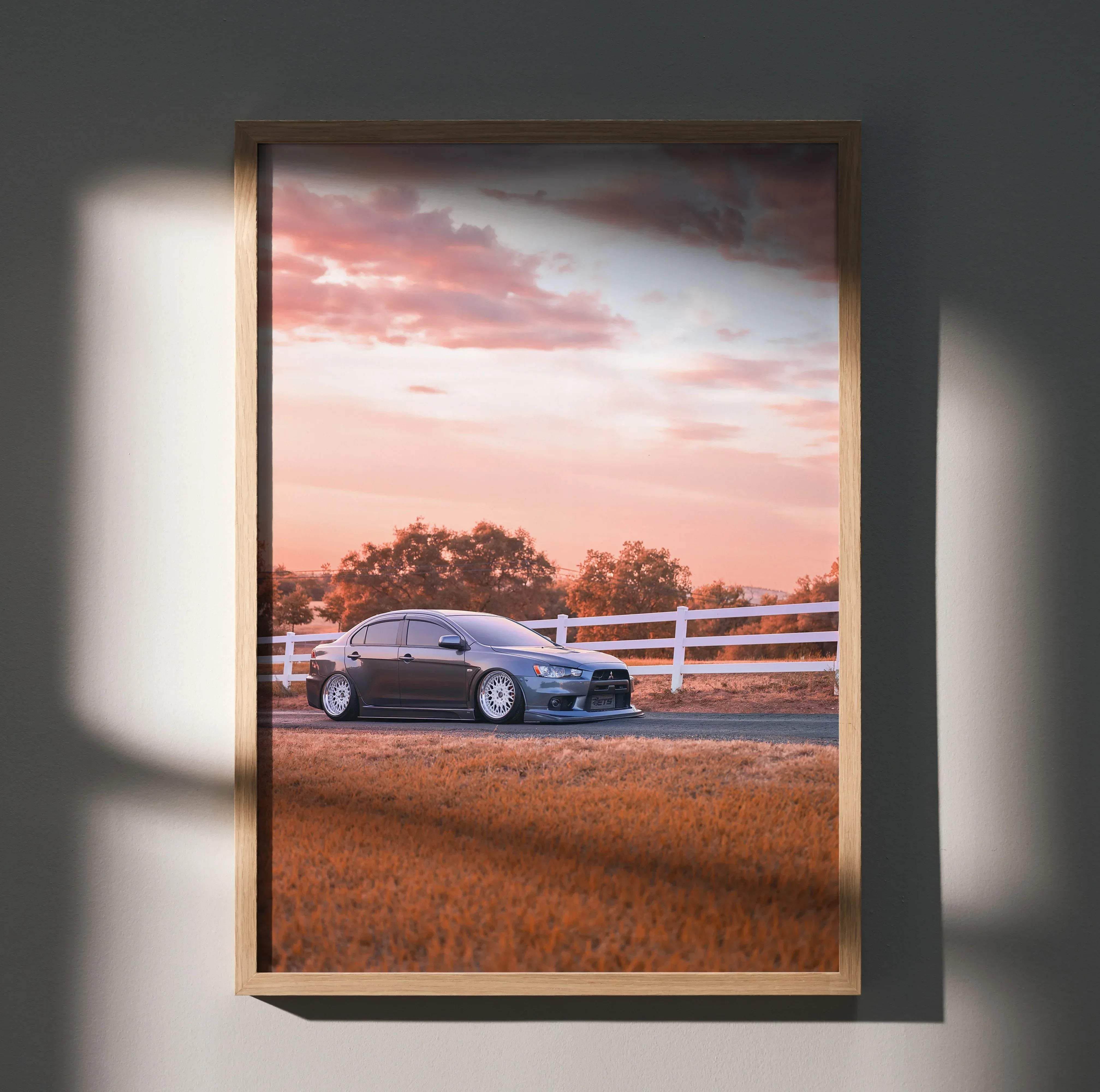 A framed high resolution poster of a dark gray mitsubishi lancer evolution 10 parked beside a white fence at sunset