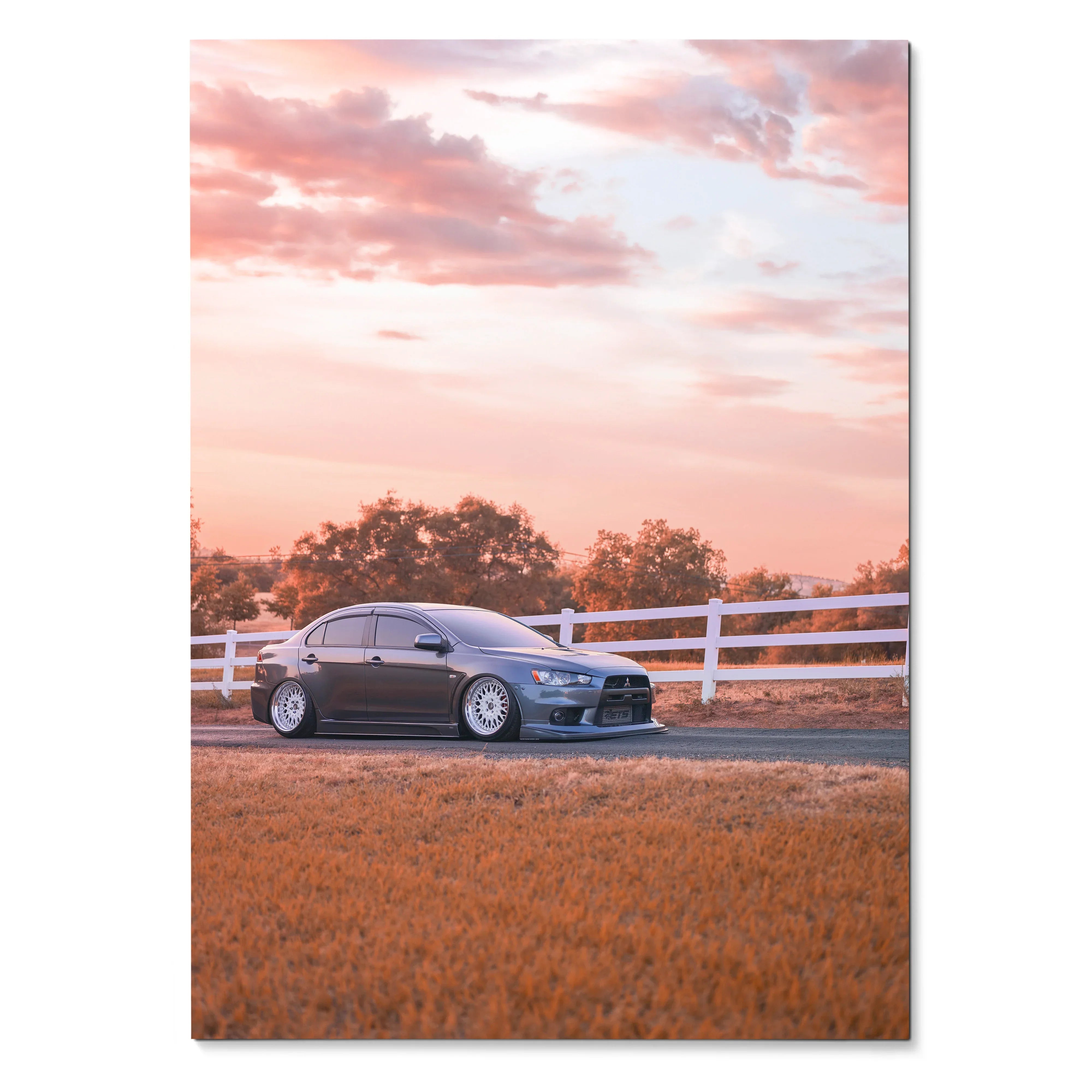 Mitsubishi Evo 10 parked by white fence at sunset poster wall art with warm sky tones.