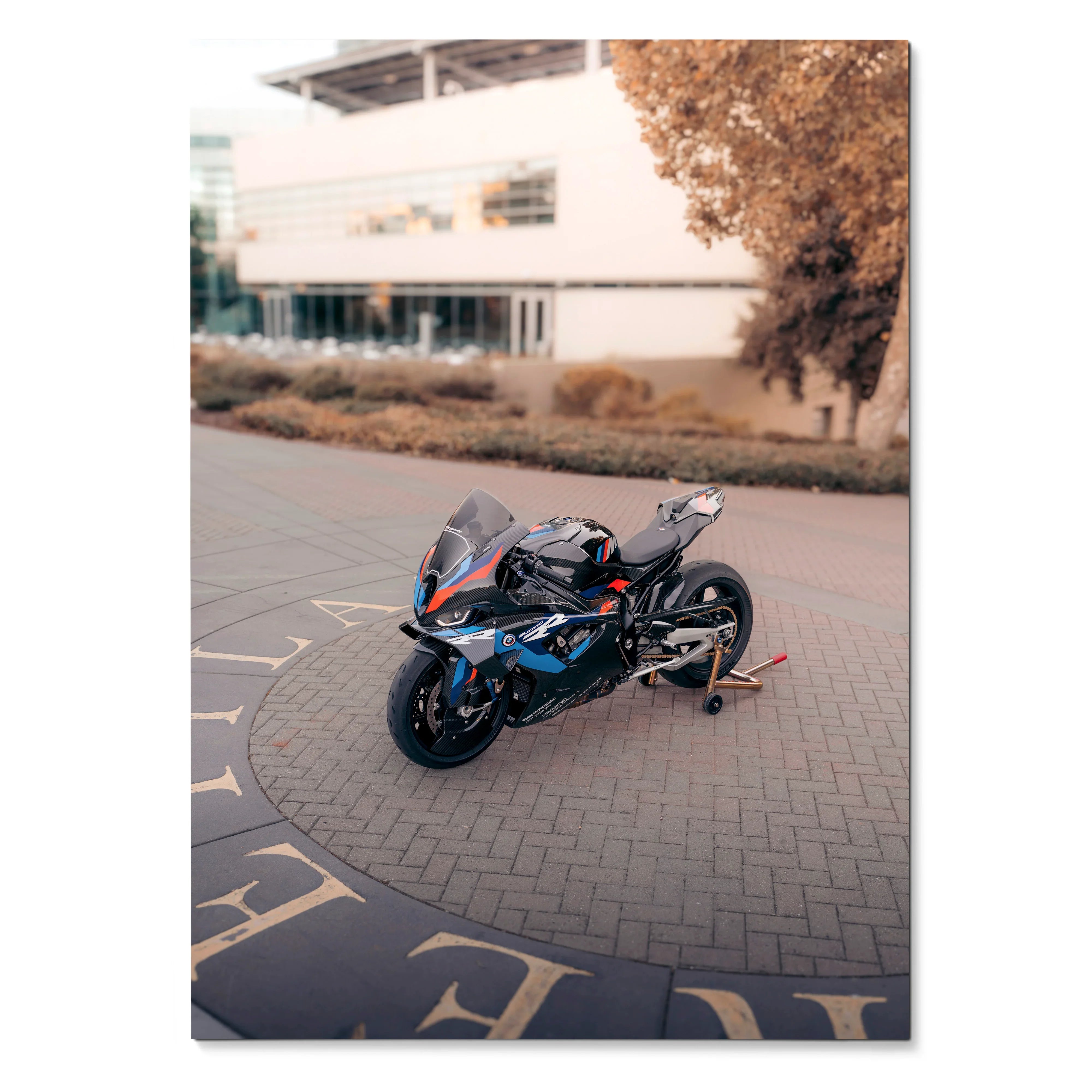 BMW M1000RR motorcycle parked on a paved road with modern building and autumn tree in the background poster wall art.