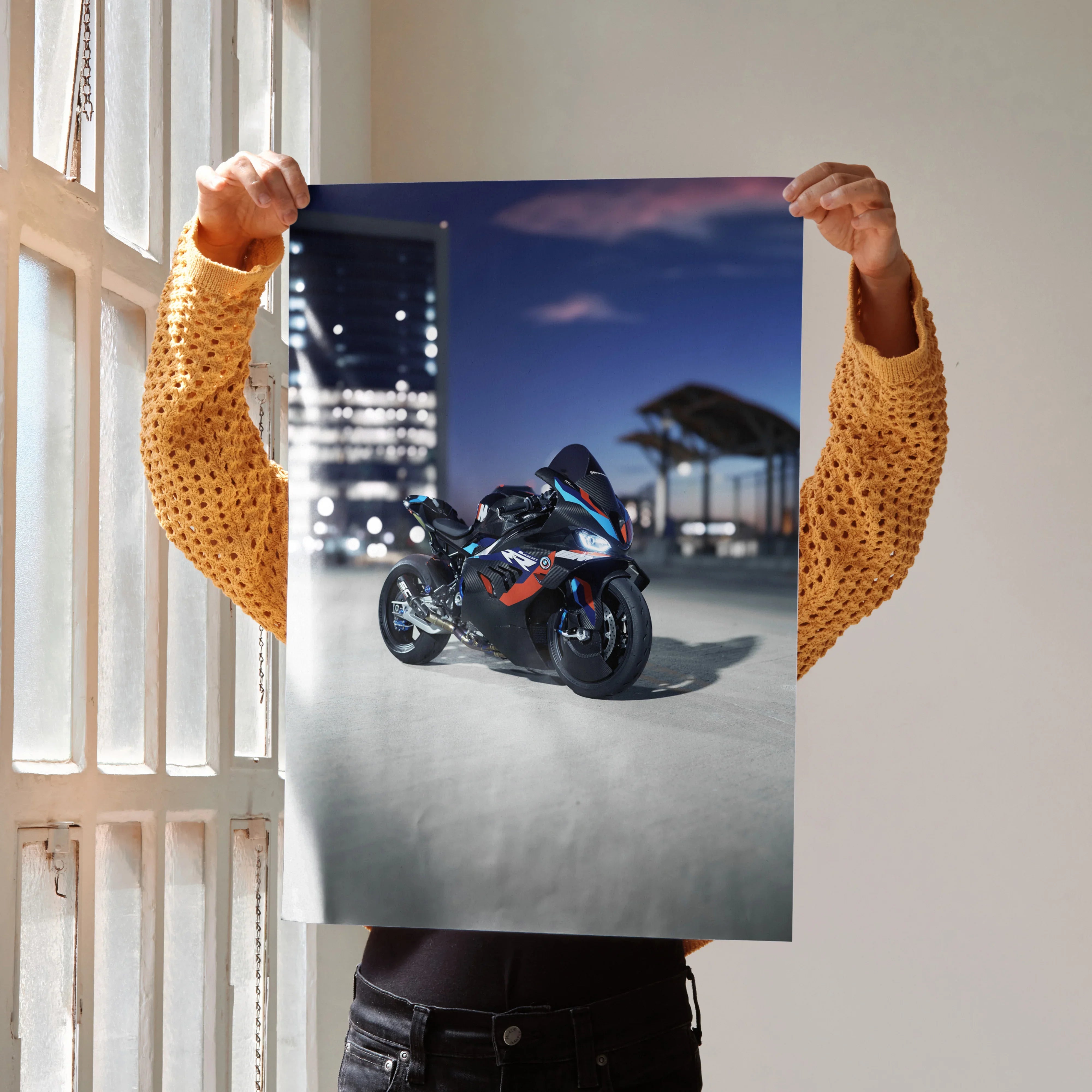 BMW M1000RR motorcycle poster wall art with night cityscape background held by person.