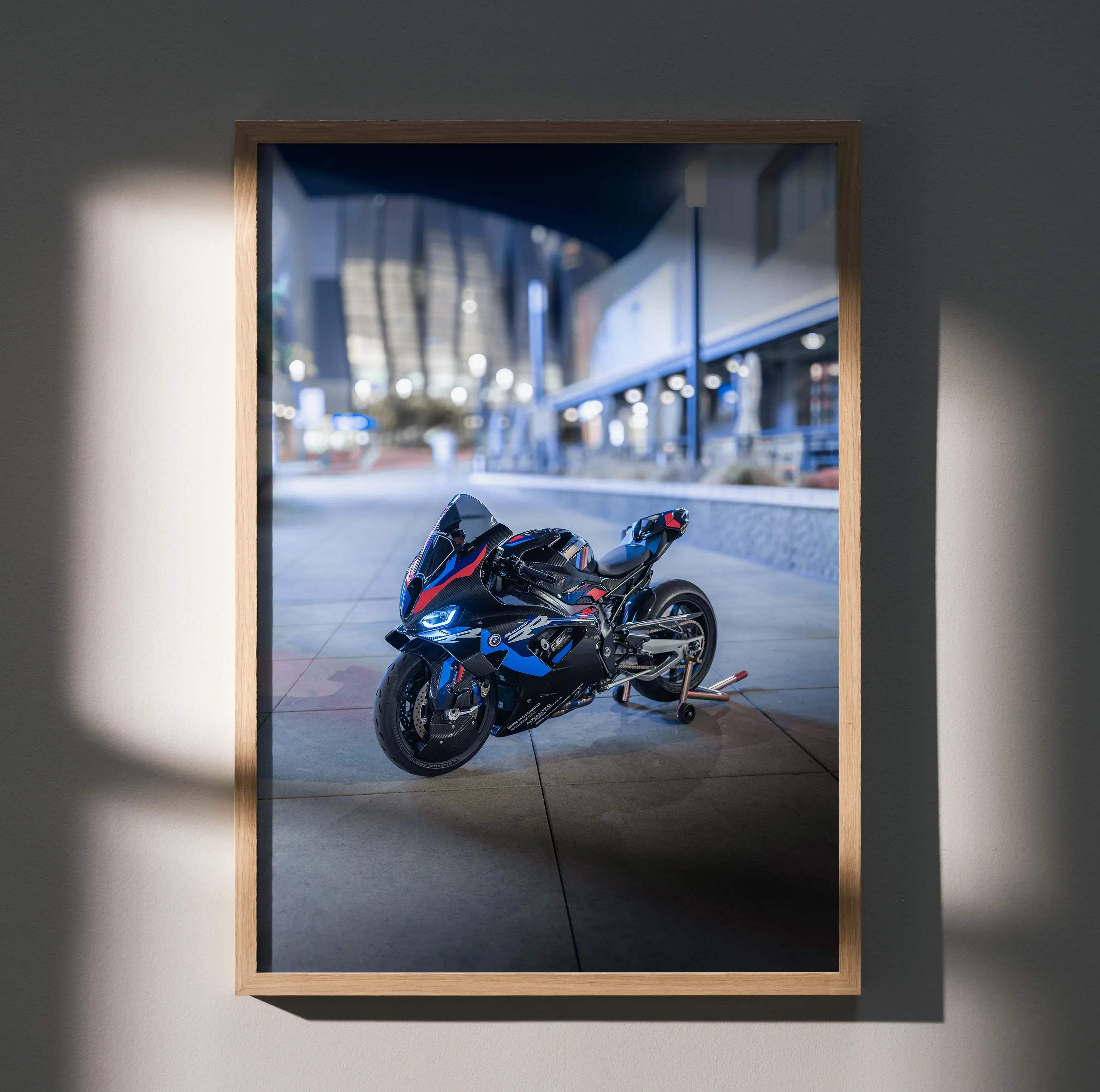 A framed photograph of a sleek blue and black BMW inspired M1000RR motorcycle with red accents in an urban night setting