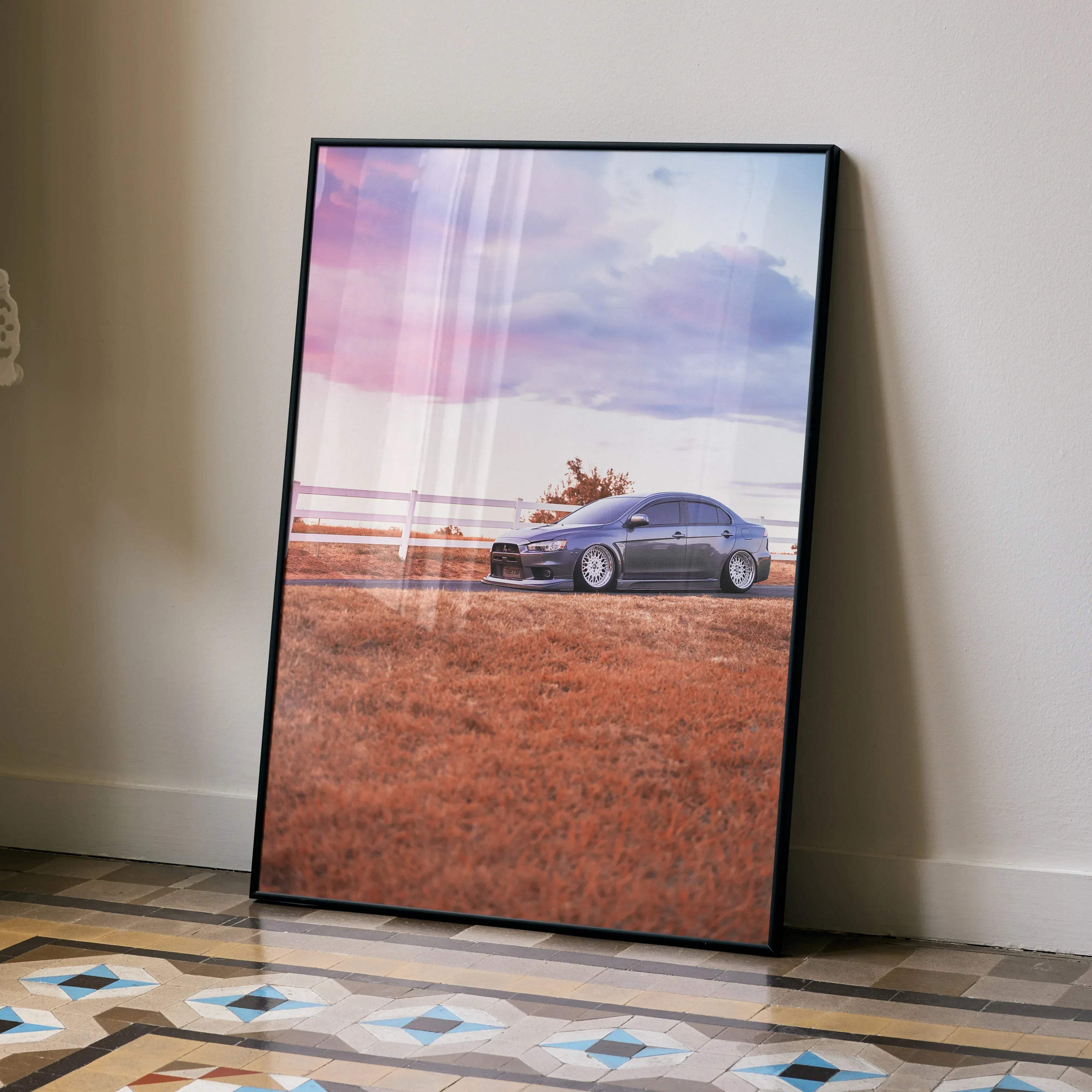 Black-framed poster of a gray mitsubishi lancer evolution parked on dirt under pink and purple sky for car decor