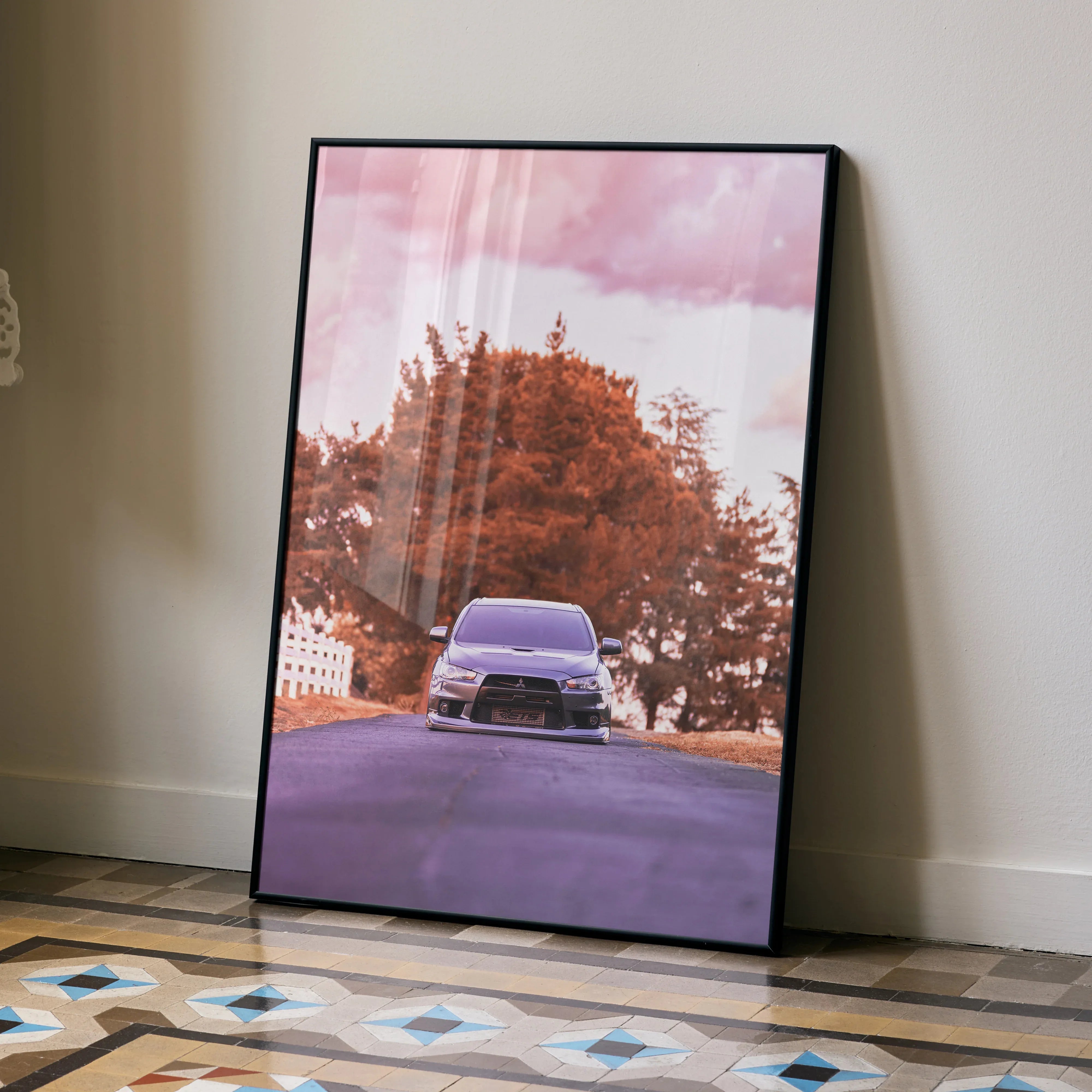 Mitsubishi Evo 10 poster with purple car and orange trees wall art in black frame, leaning on floor.