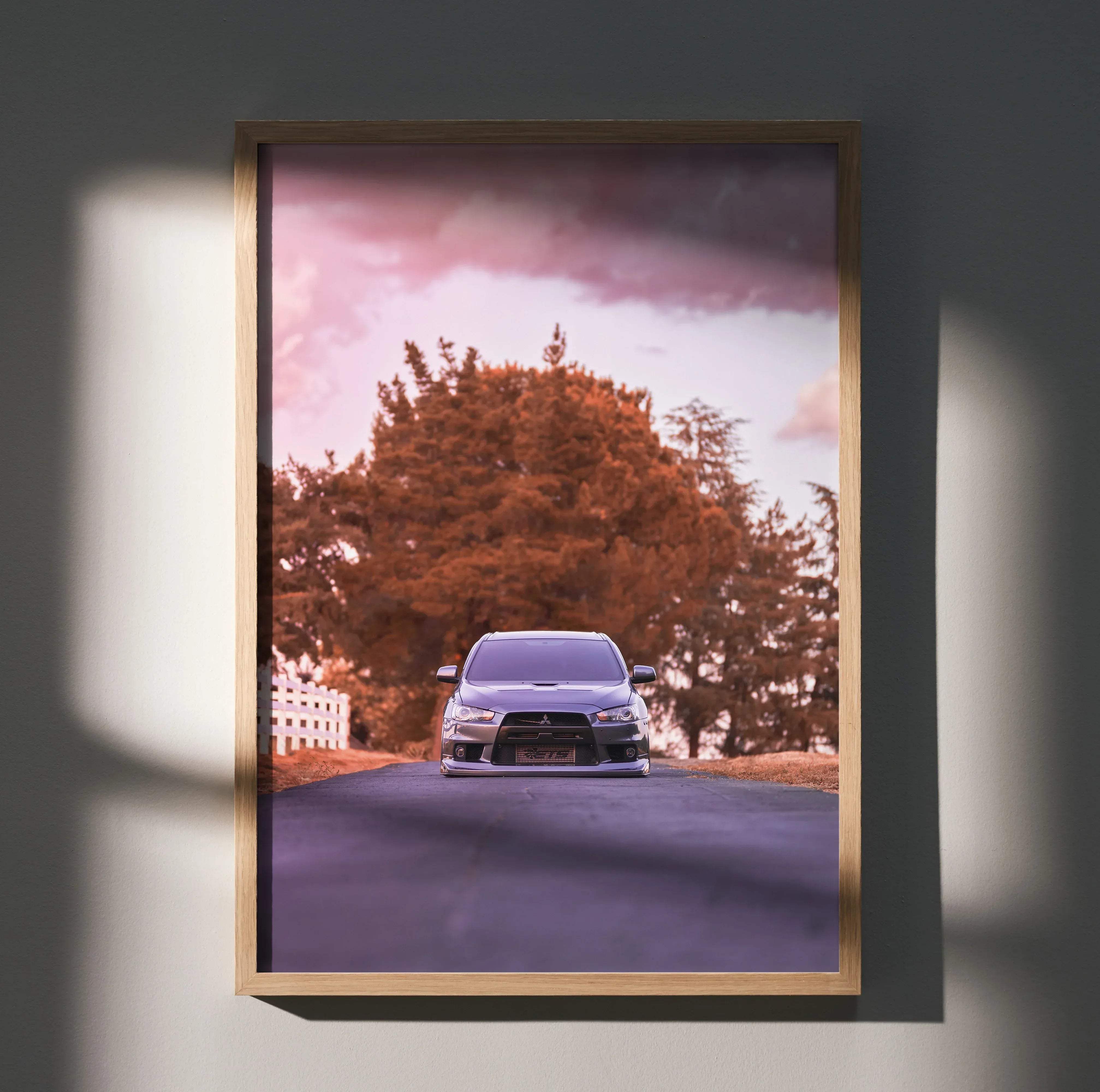 A framed Mitsubishi Evo 10 high resolution silver sports car poster driving down a tree-lined road at sunset