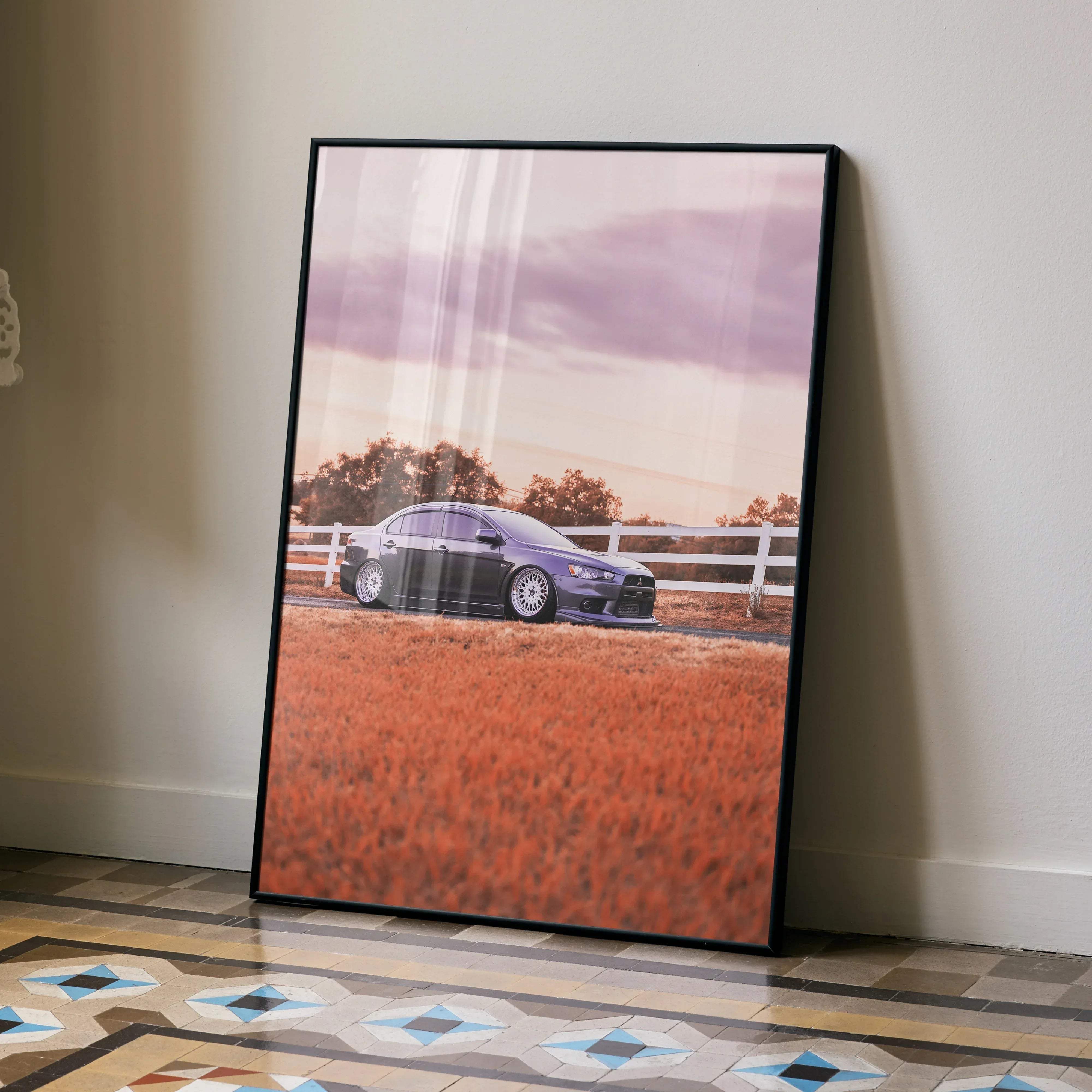 Black-framed poster featuring a purple mitsubishi lancer evolution 10 parked in a field with a white fence under a pink sky