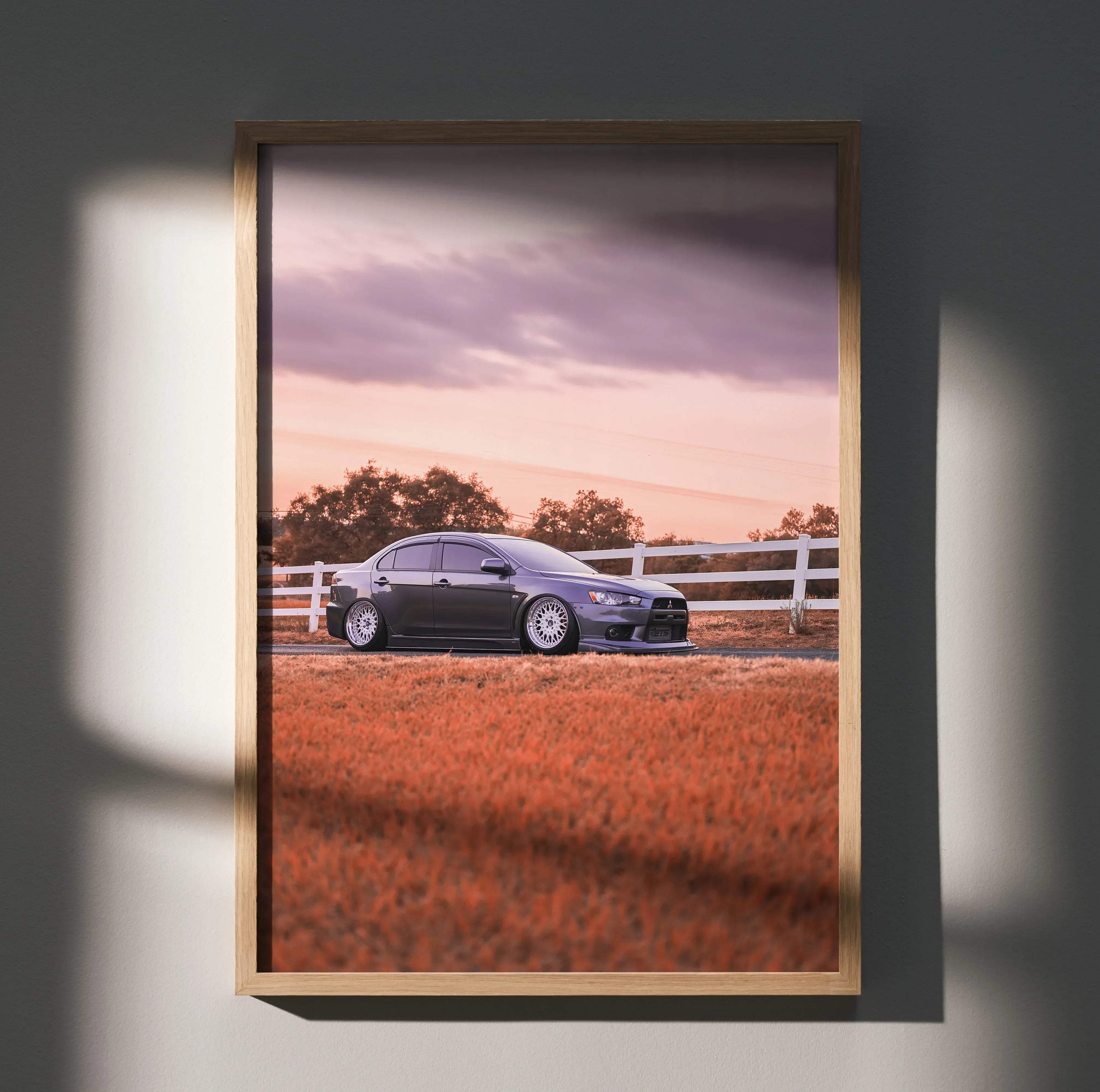 A framed high resolution poster of a dark gray Mitsubishi Lancer Evolution parked in a field at sunset