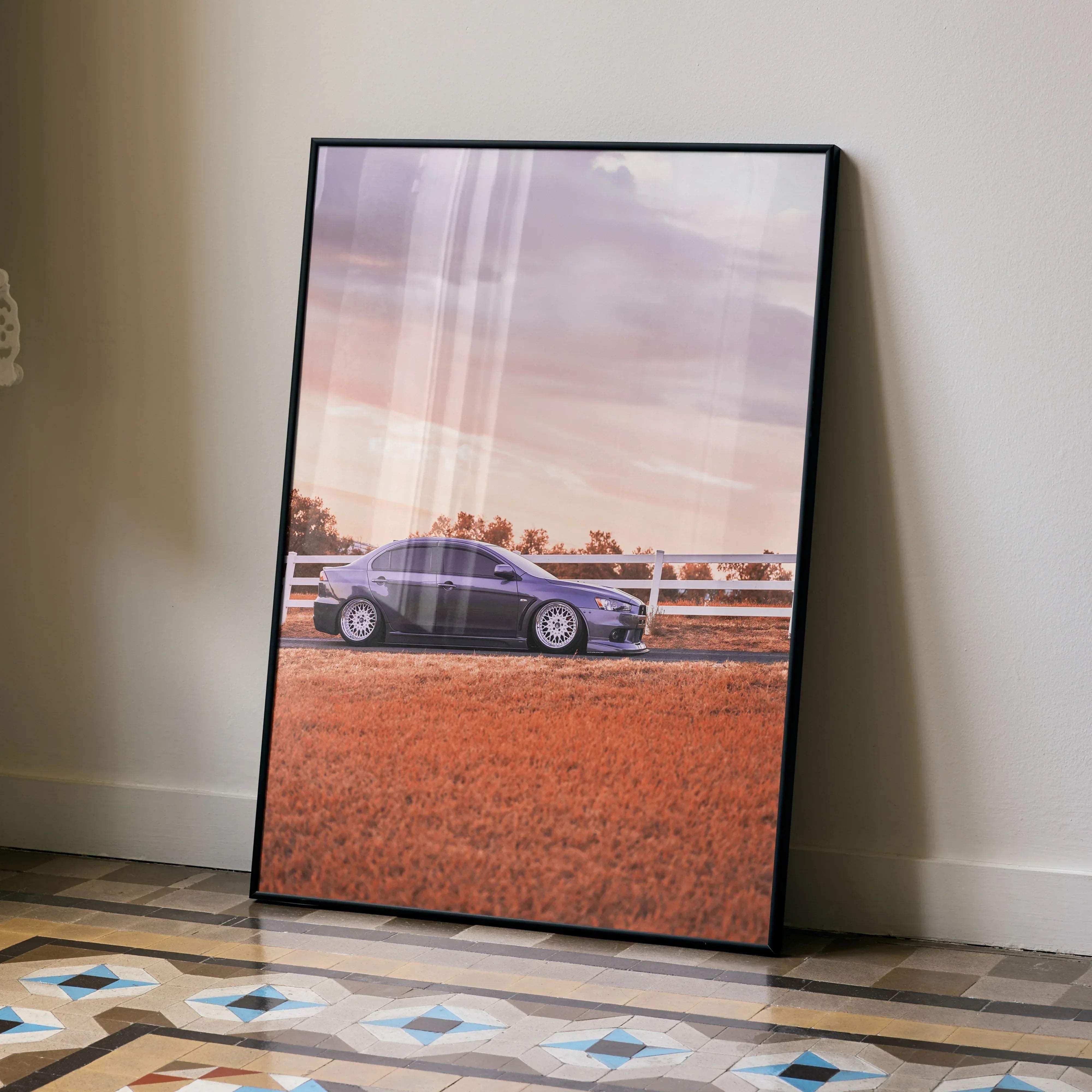 Black-framed poster of a purple mitsubishi evo 10 sports car in a field with a white fence under a pastel sky