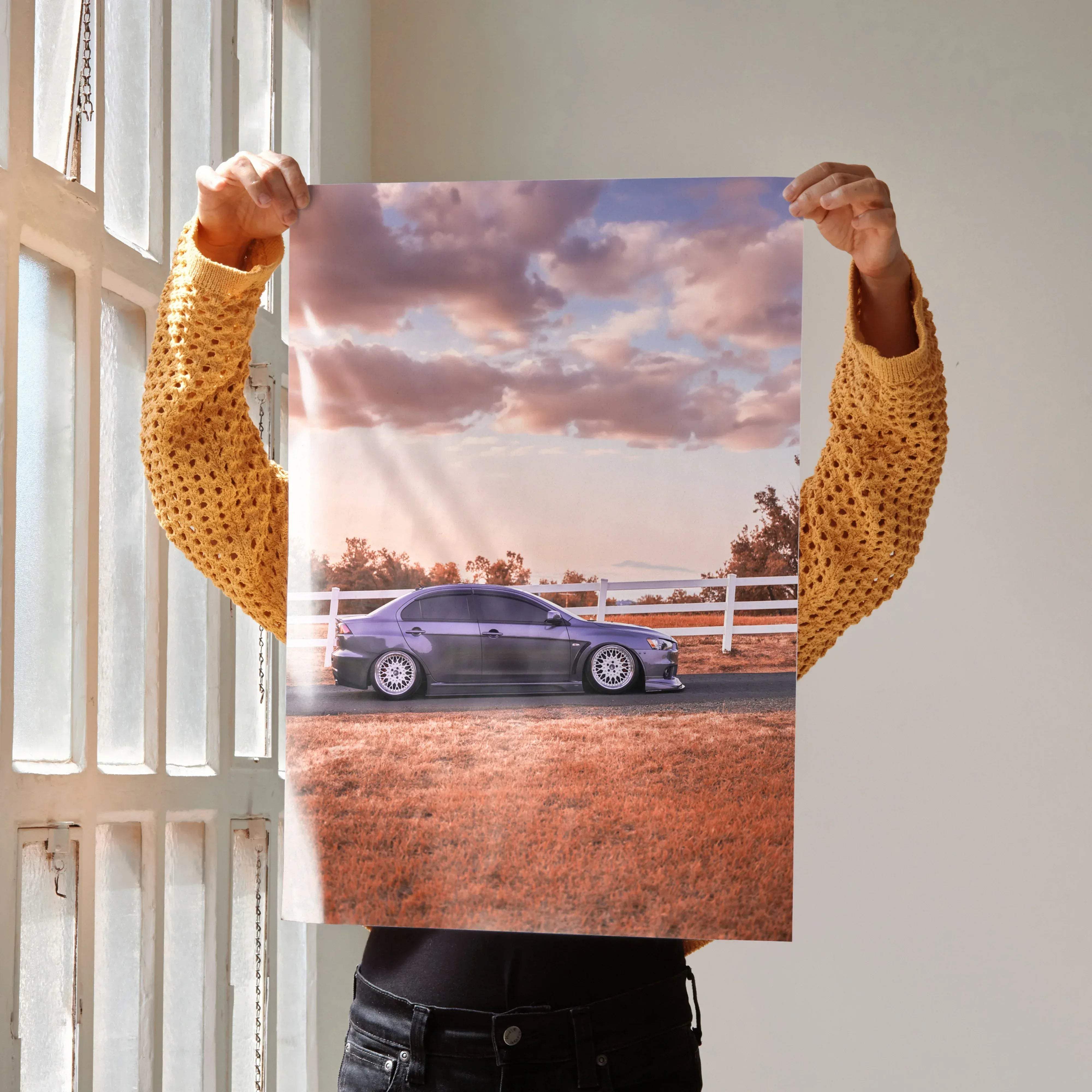 A printed poster of a sleek dark gray mitsubishi evo 10 with custom white rims under a pink and purple sky