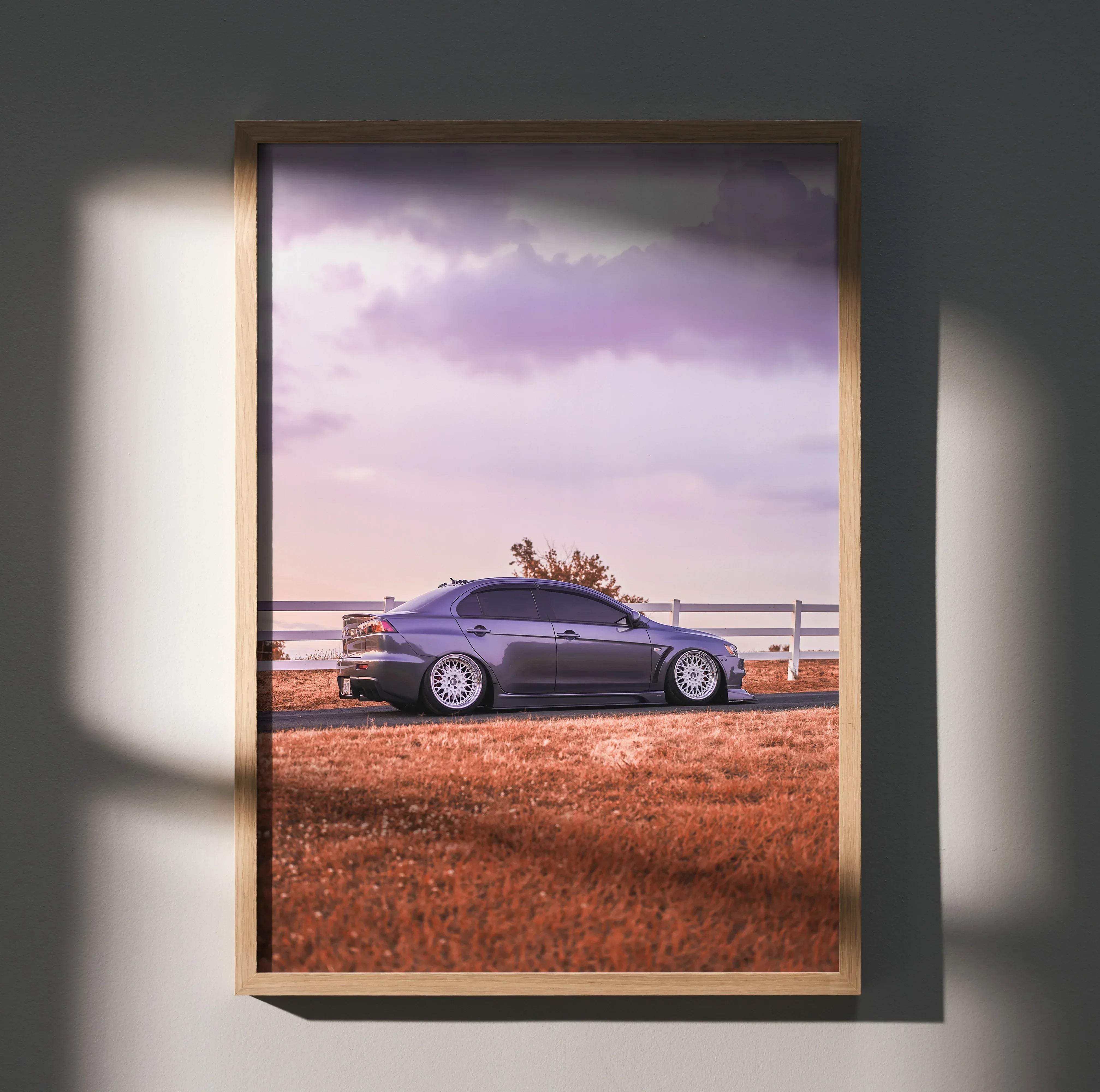 A framed high resolution poster of a dark gray Mitsubishi Evo 10 sedan parked by roadside with golden grass and purple skies
