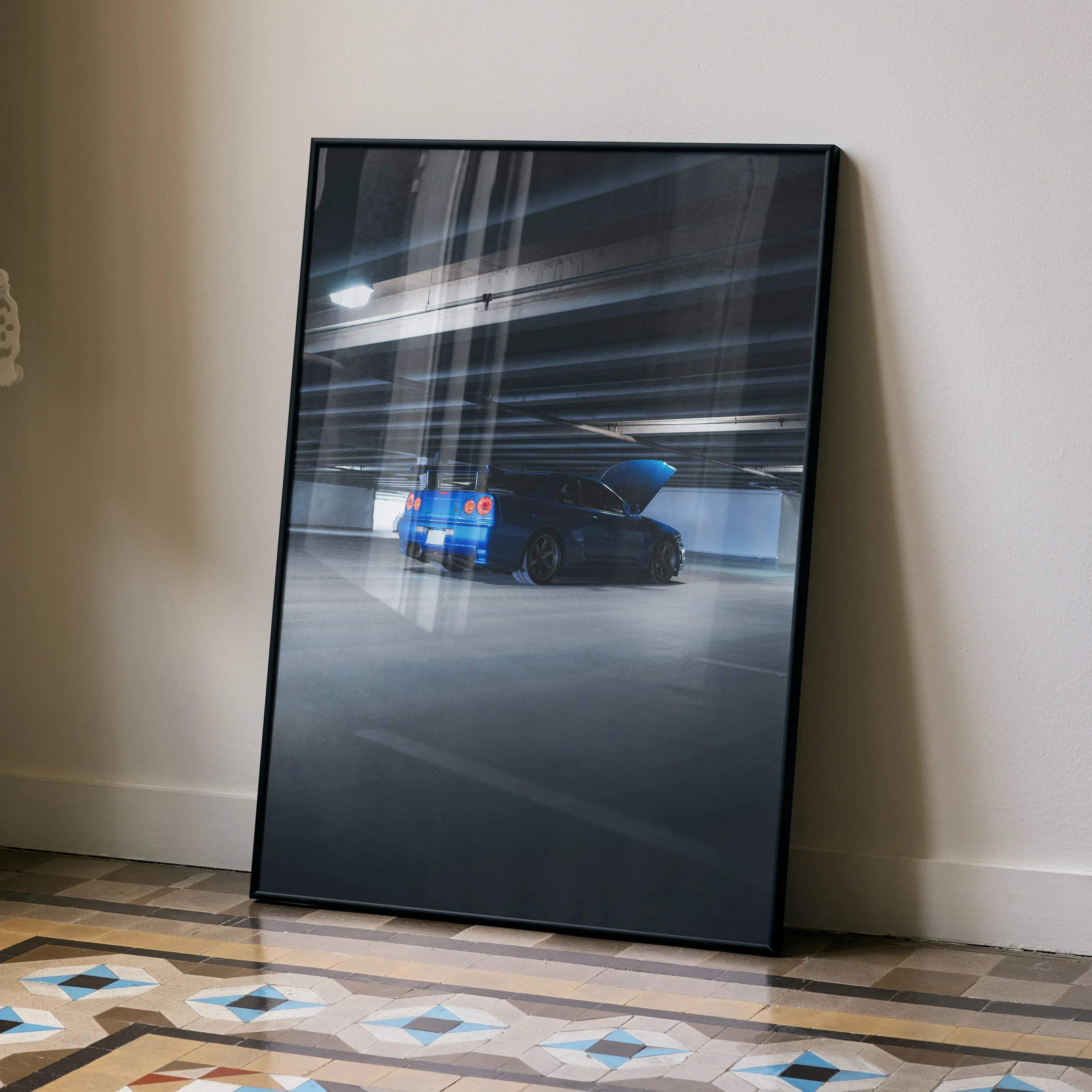 Black-framed photographic print of blue nissan r34 gtr skyline with hood open in underground garage car poster