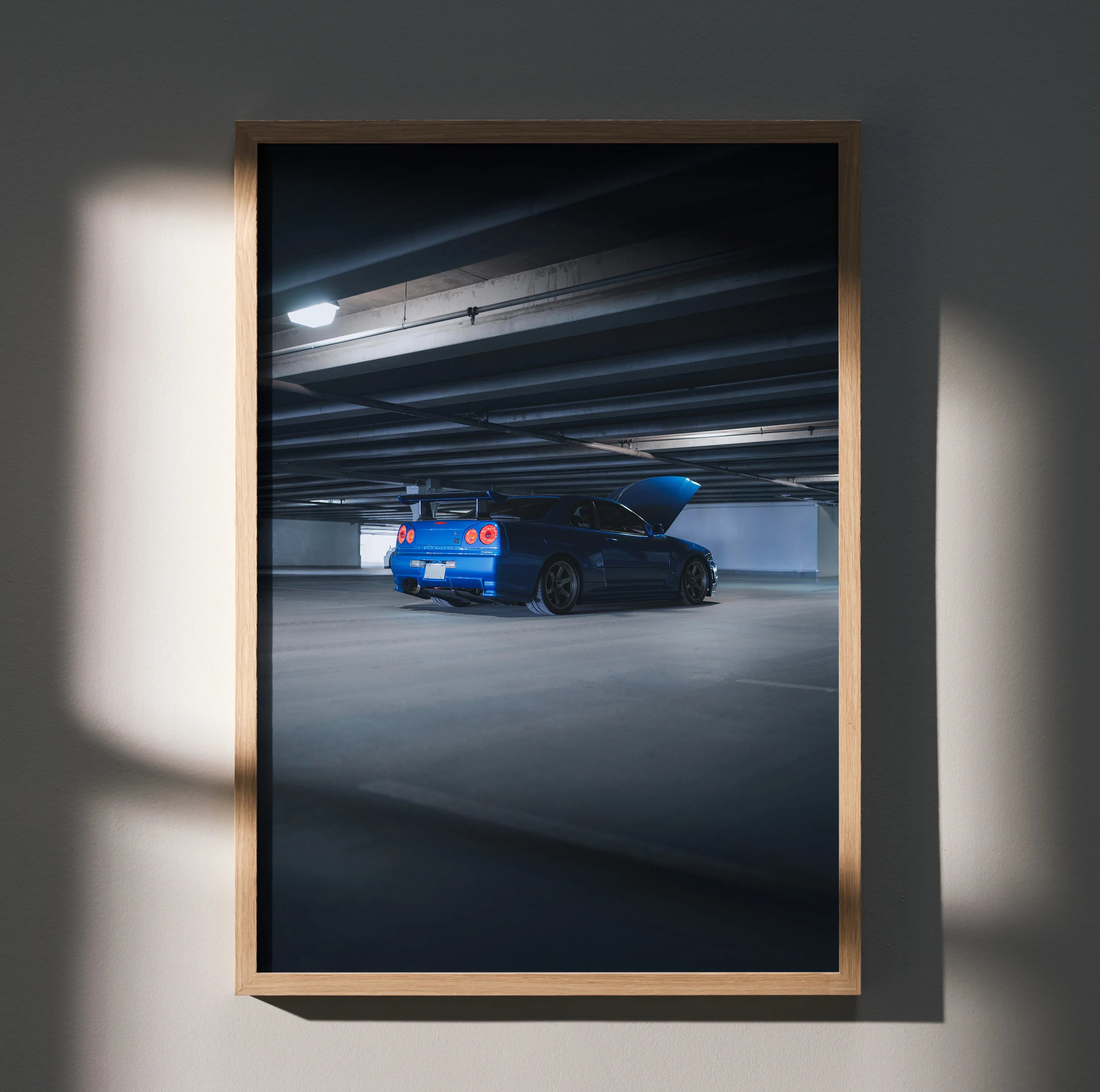 Nissan R34 GTR in blue under dim parking garage lights poster wall art in wooden frame.