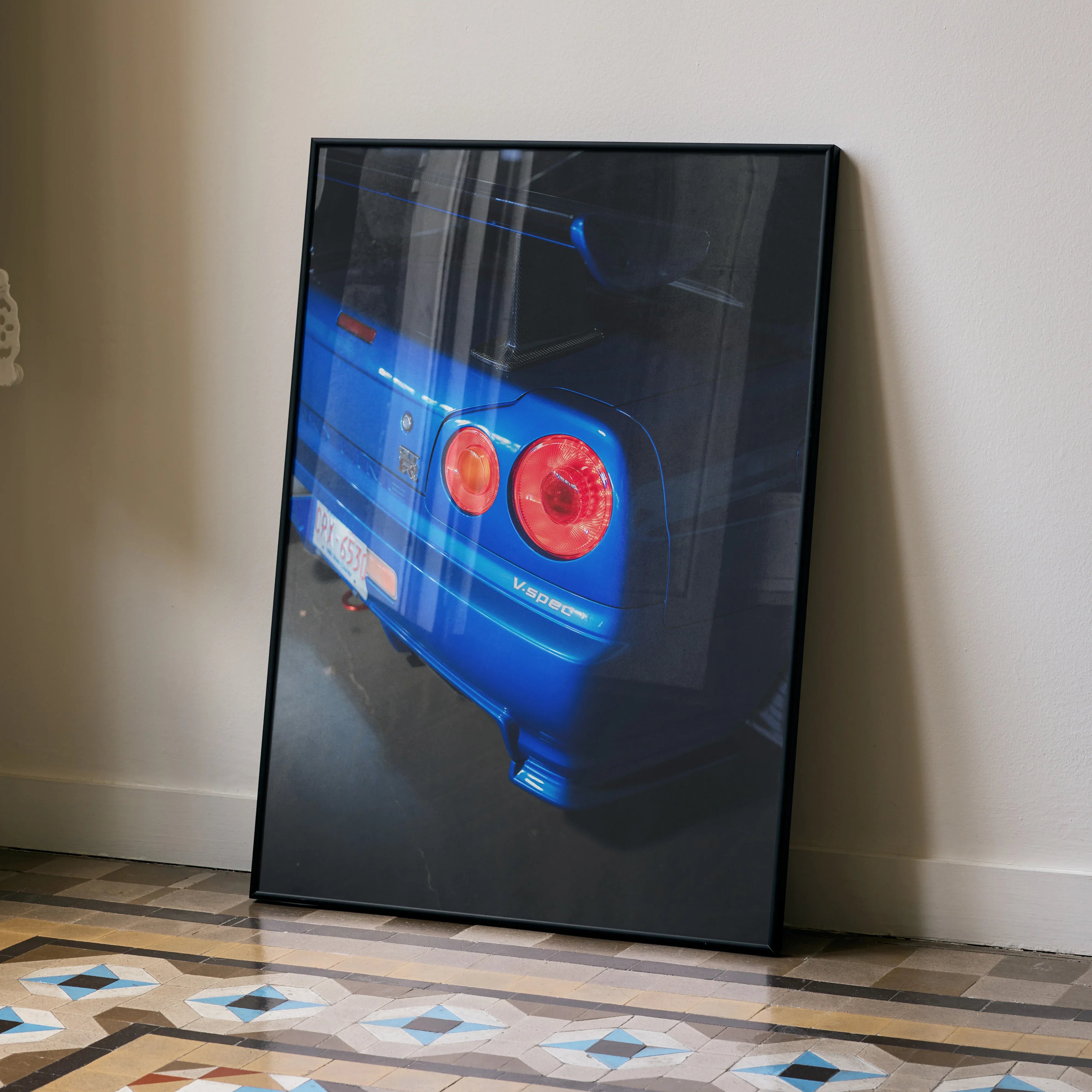 Nissan R34 GTR Skyline rear close-up poster wall art in black frame leaning on beige wall.