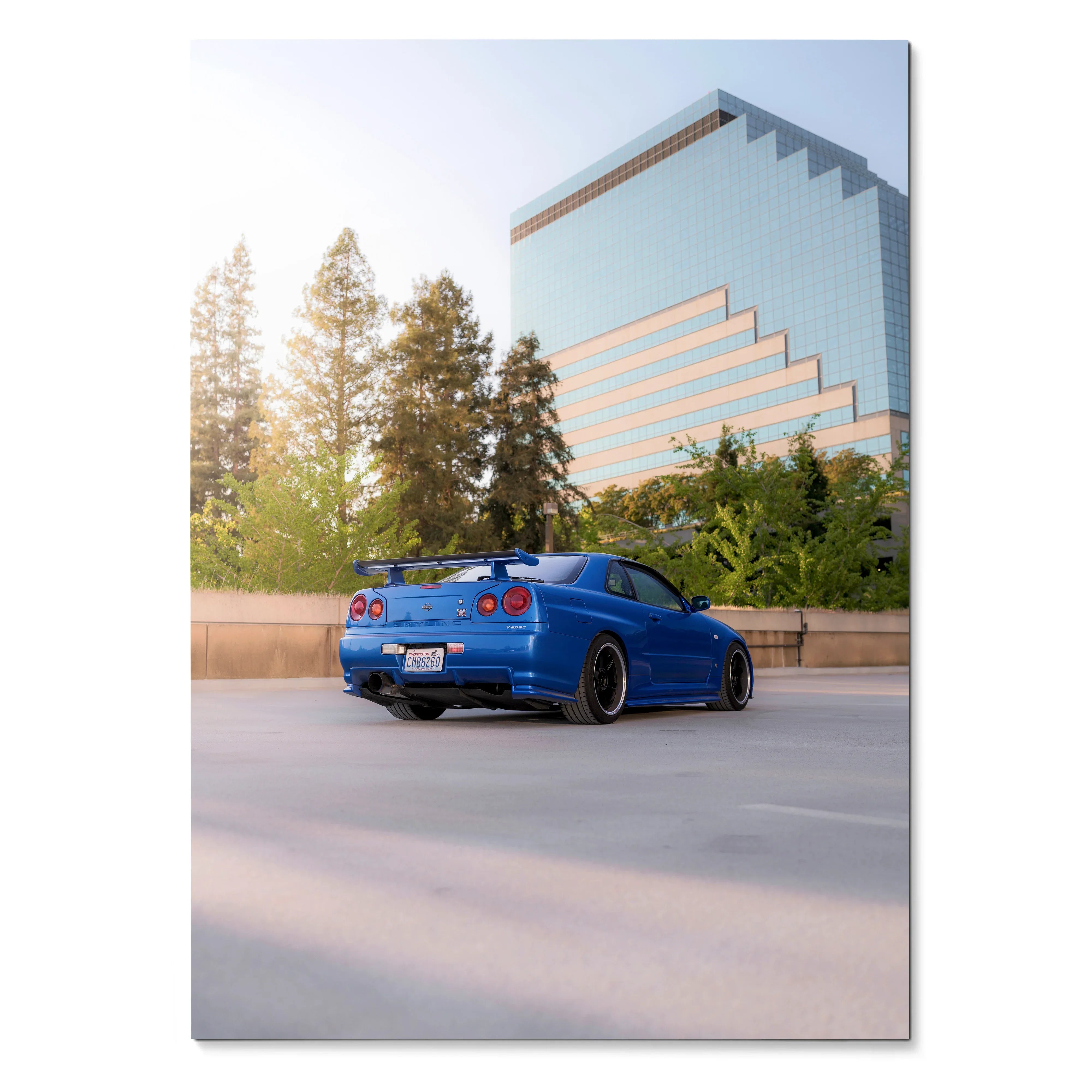 Blue Nissan R34 GTR Skyline parked by modern glass building poster wall art.