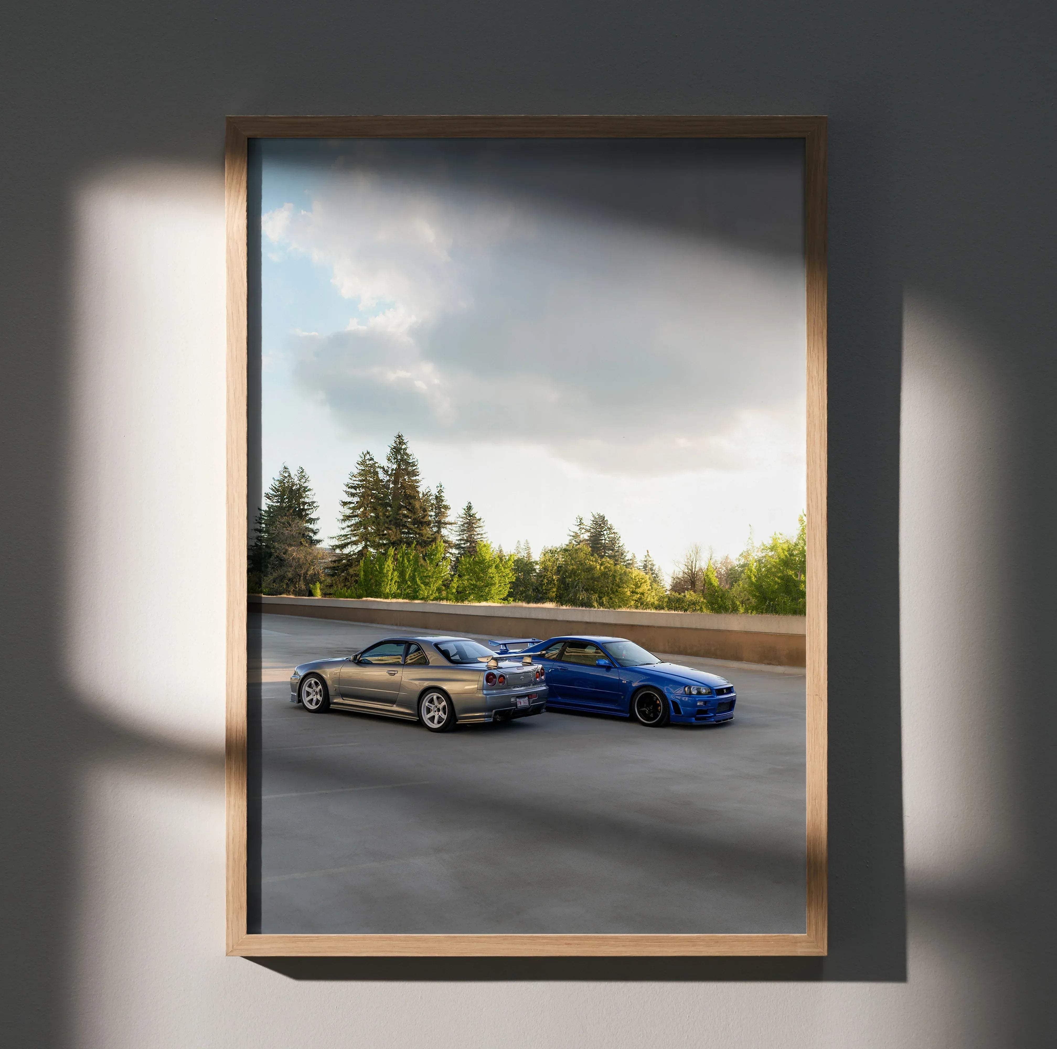 Framed artwork of silver and blue nissan skyline r34 gtrs parked on asphalt road with trees in background car poster