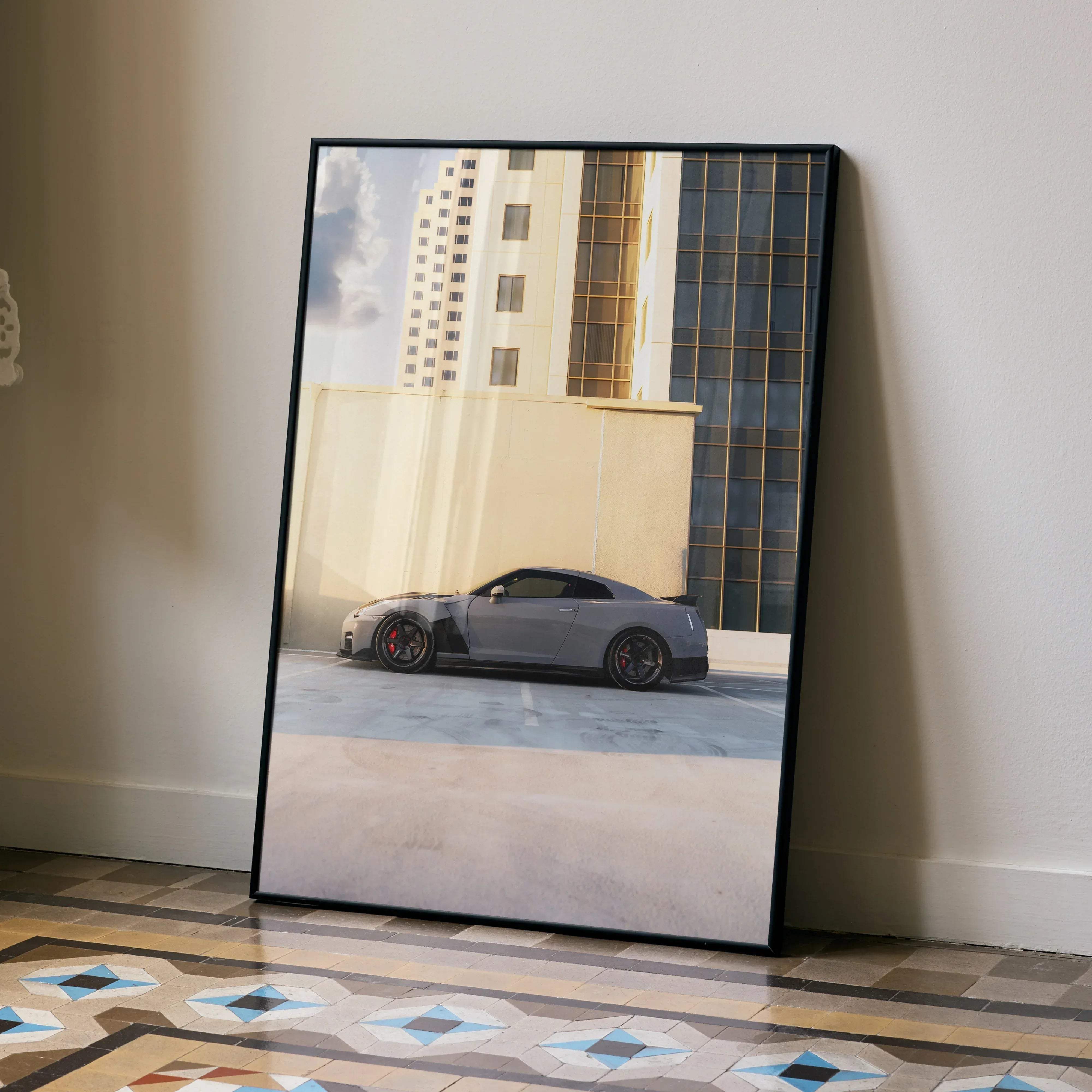 A framed high resolution poster of a sleek gray Nissan GTR R35 sports car with red brake calipers parked by a beige wall