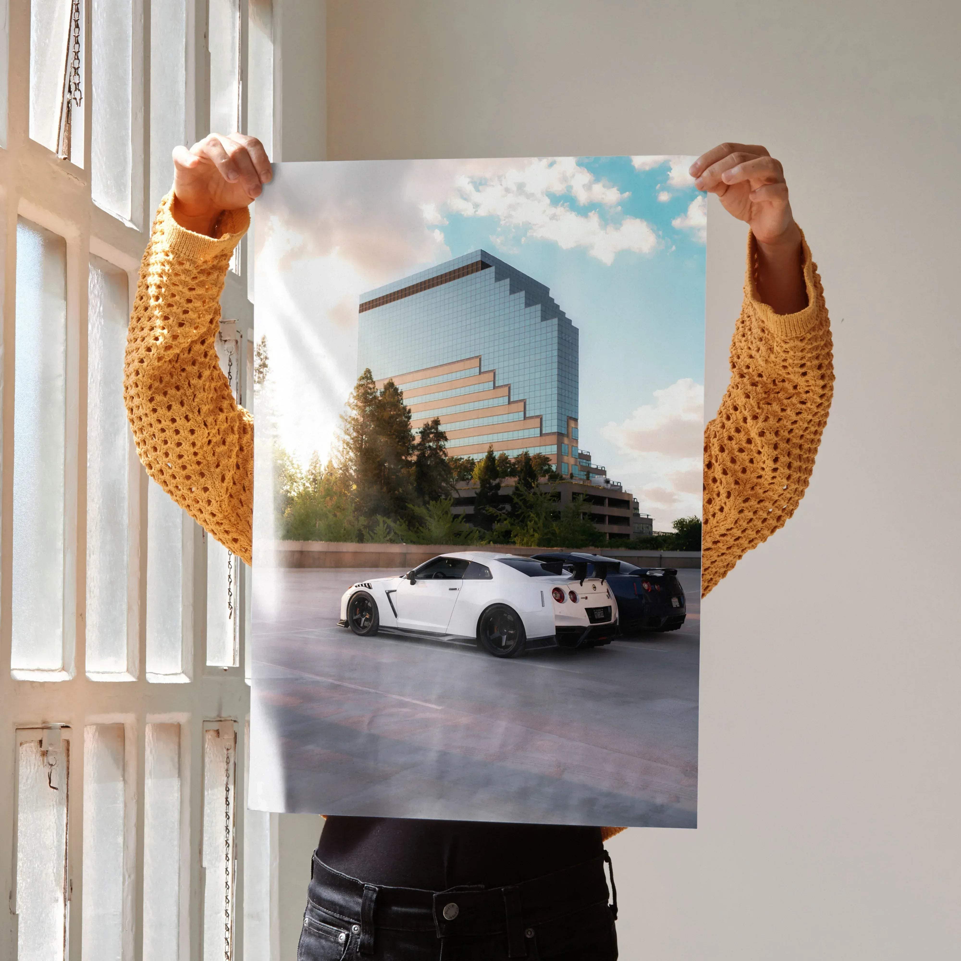 White Nissan GT-R R35 sports car with black rims parked in front of a modern glass building high resolution poster
