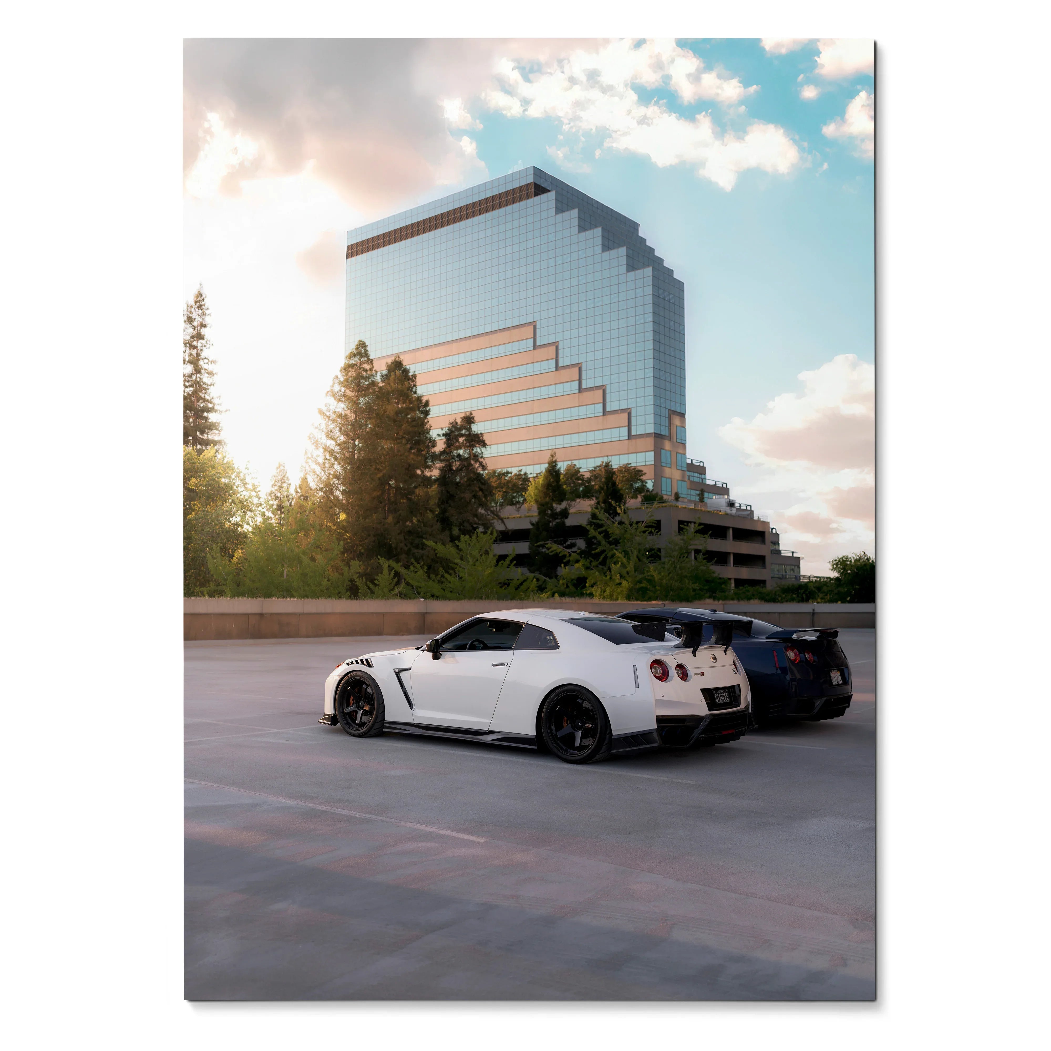 Nissan GTR R35 poster featuring white and black cars parked by modern stepped glass building under cloudy sky wall art.