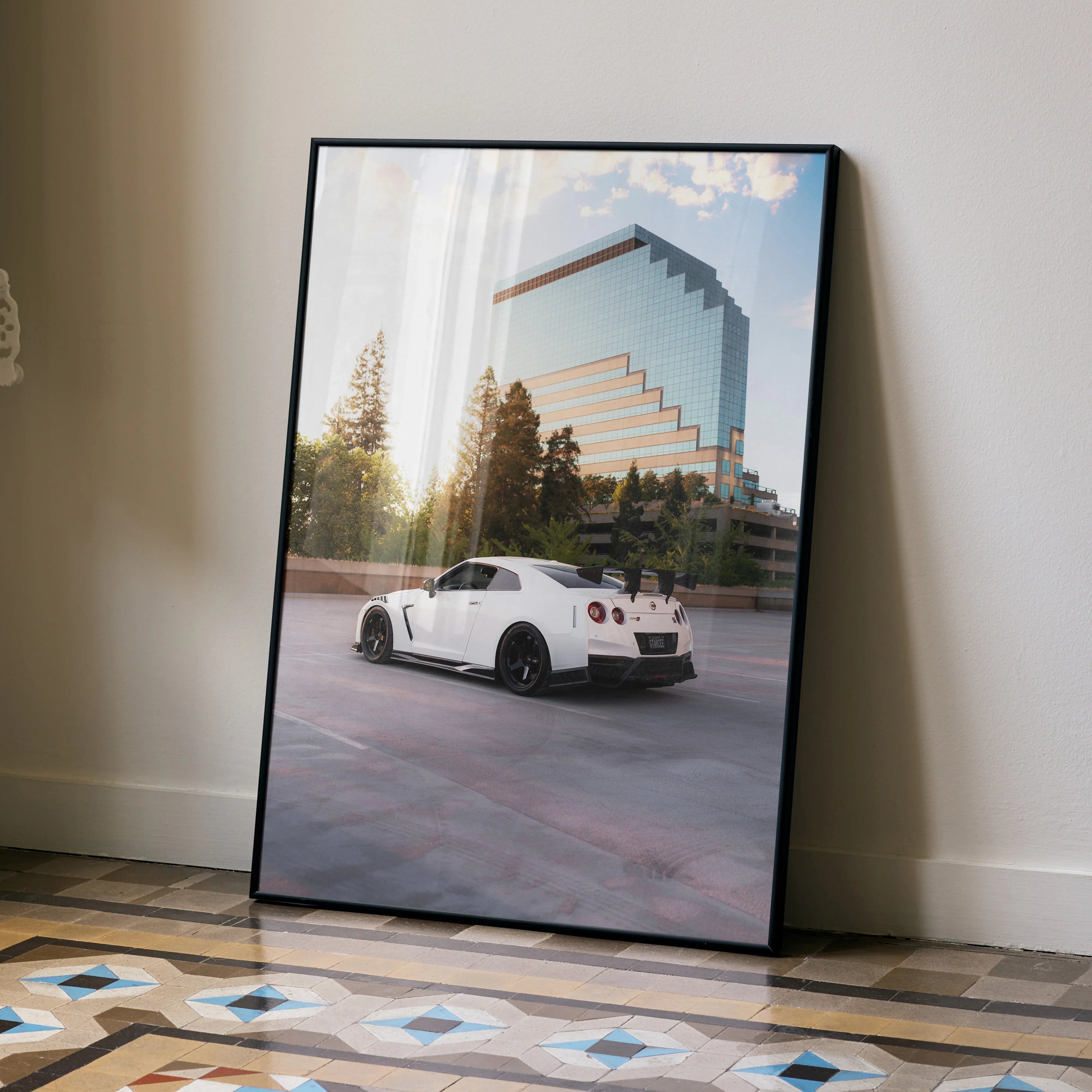 Nissan GTR R35 white sports car poster leaning on wall with modern glass building and trees in background wall art.