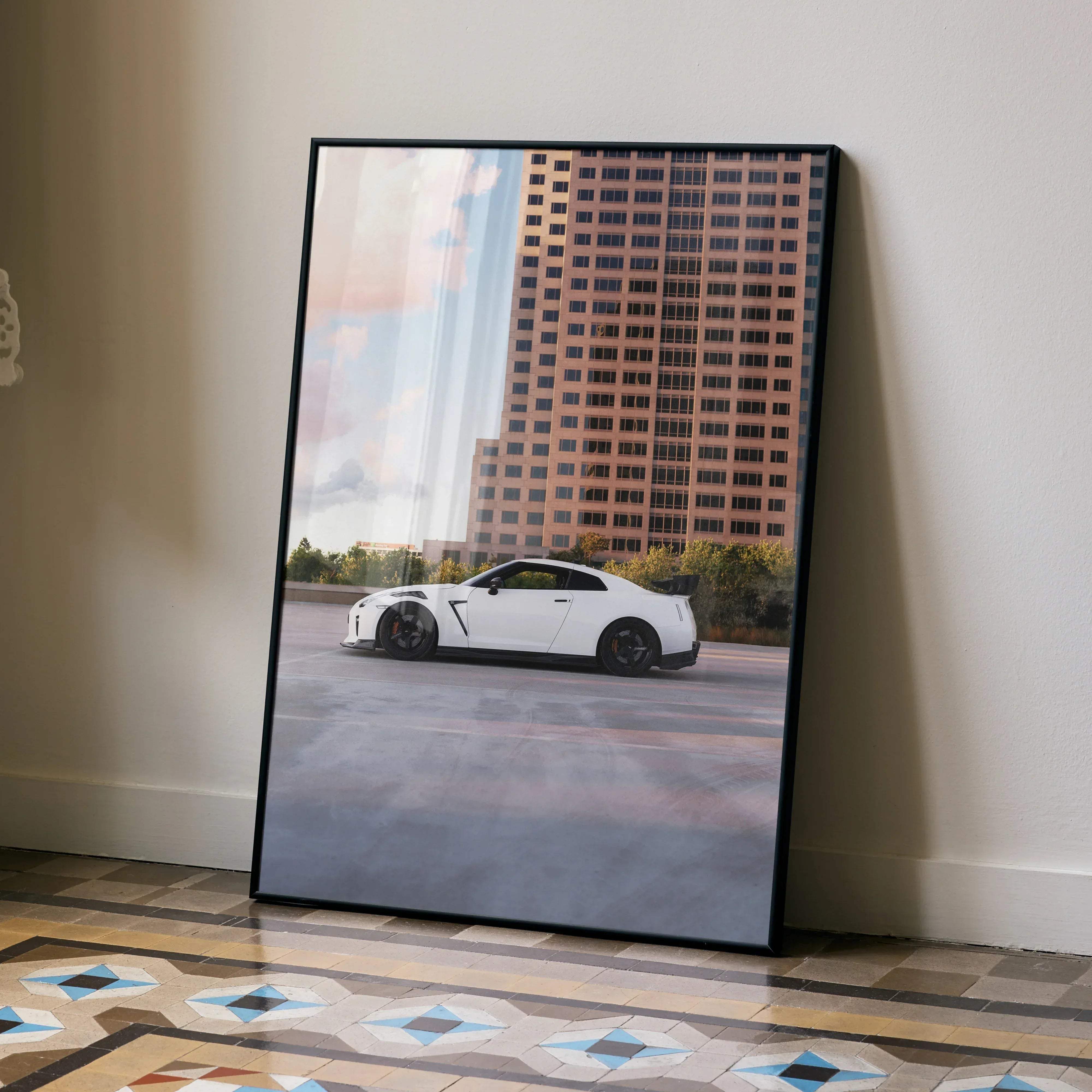 Black-framed poster featuring a white Nissan GT-R R35 sports car parked in front of a tall building high resolution