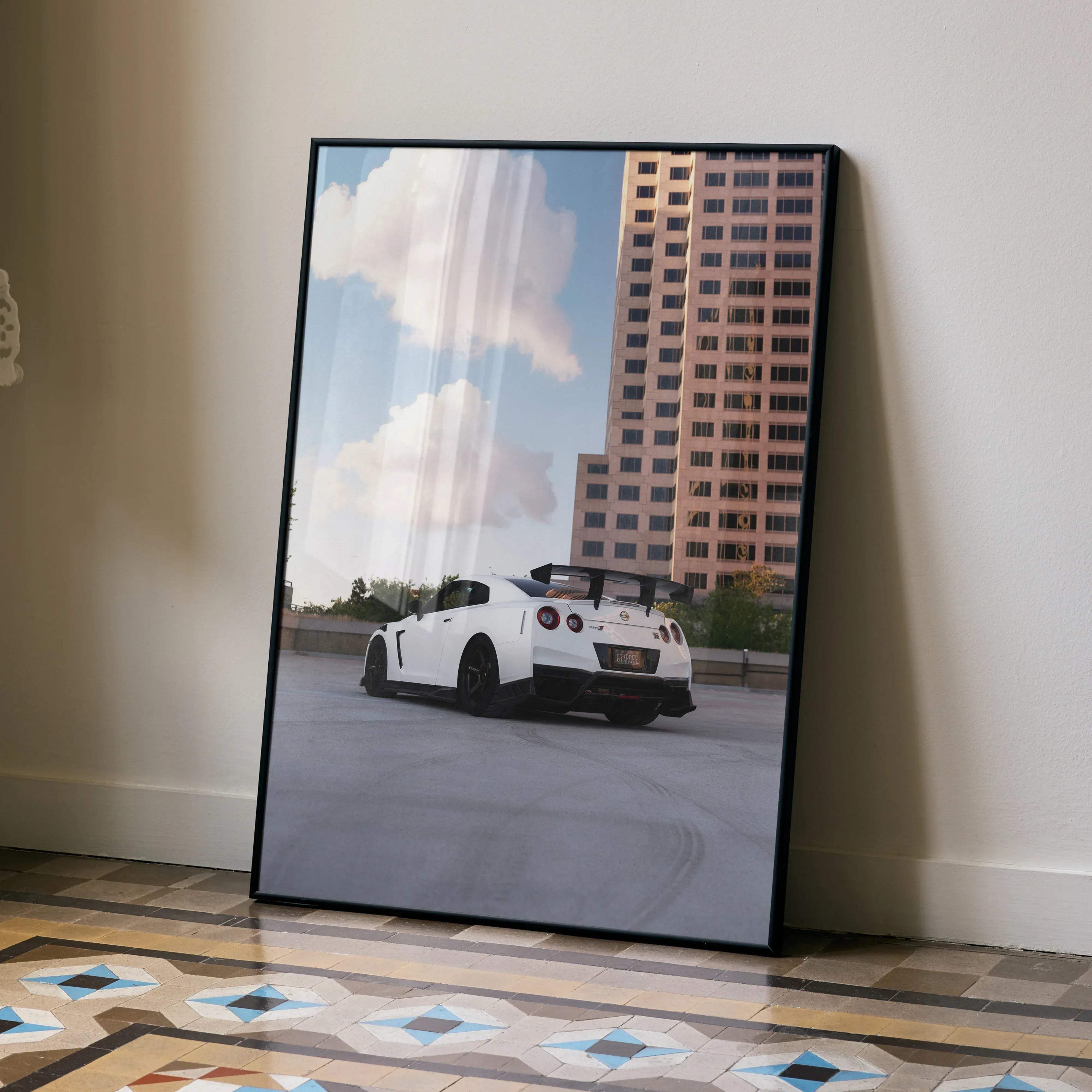 Black-framed poster of a white nissan gt-r r35 sports car with black rims and spoiler parked by tall buildings